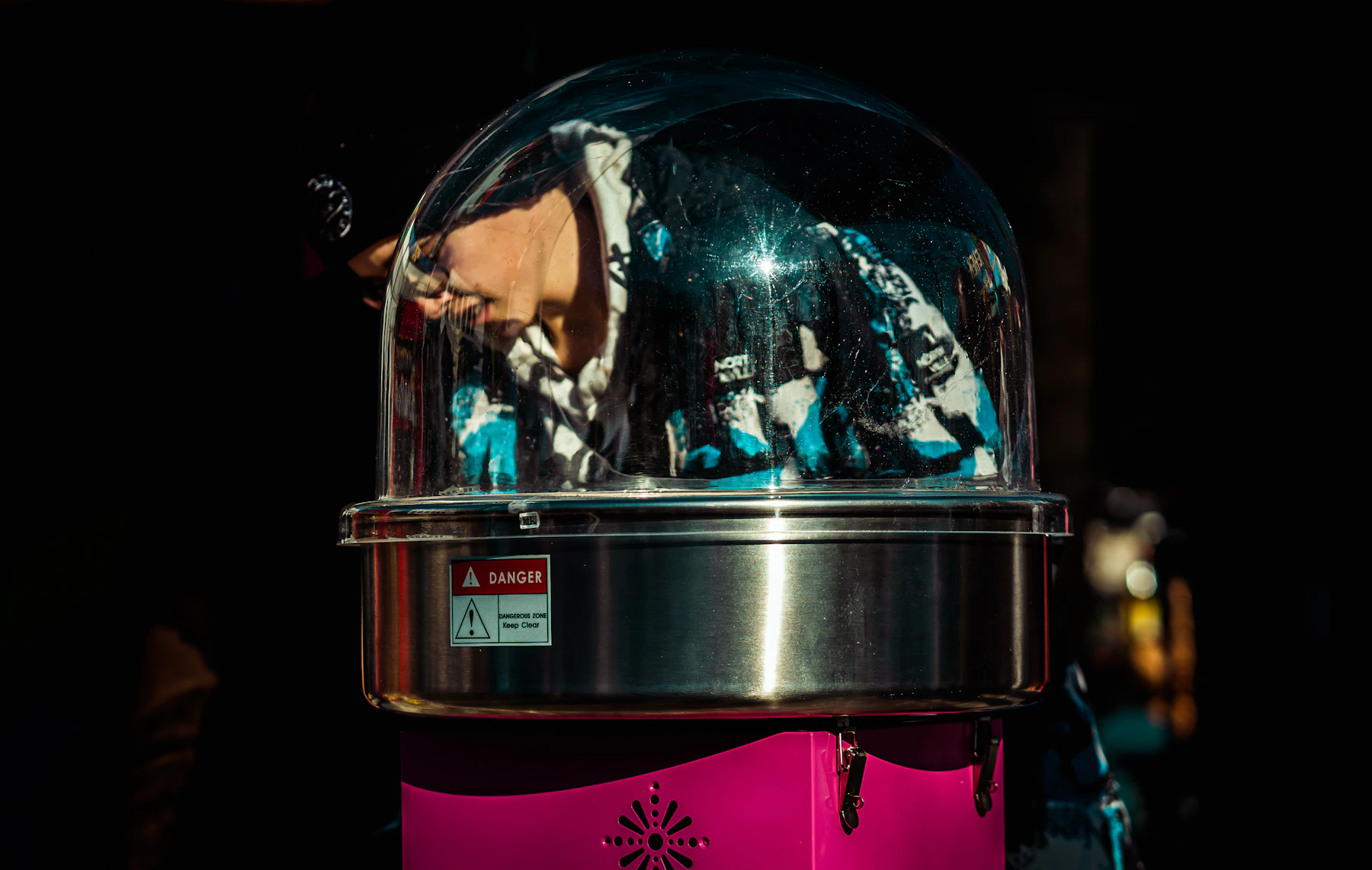 A cotton candy machine with a clear dome shield over a steel bowl on a bright pink base