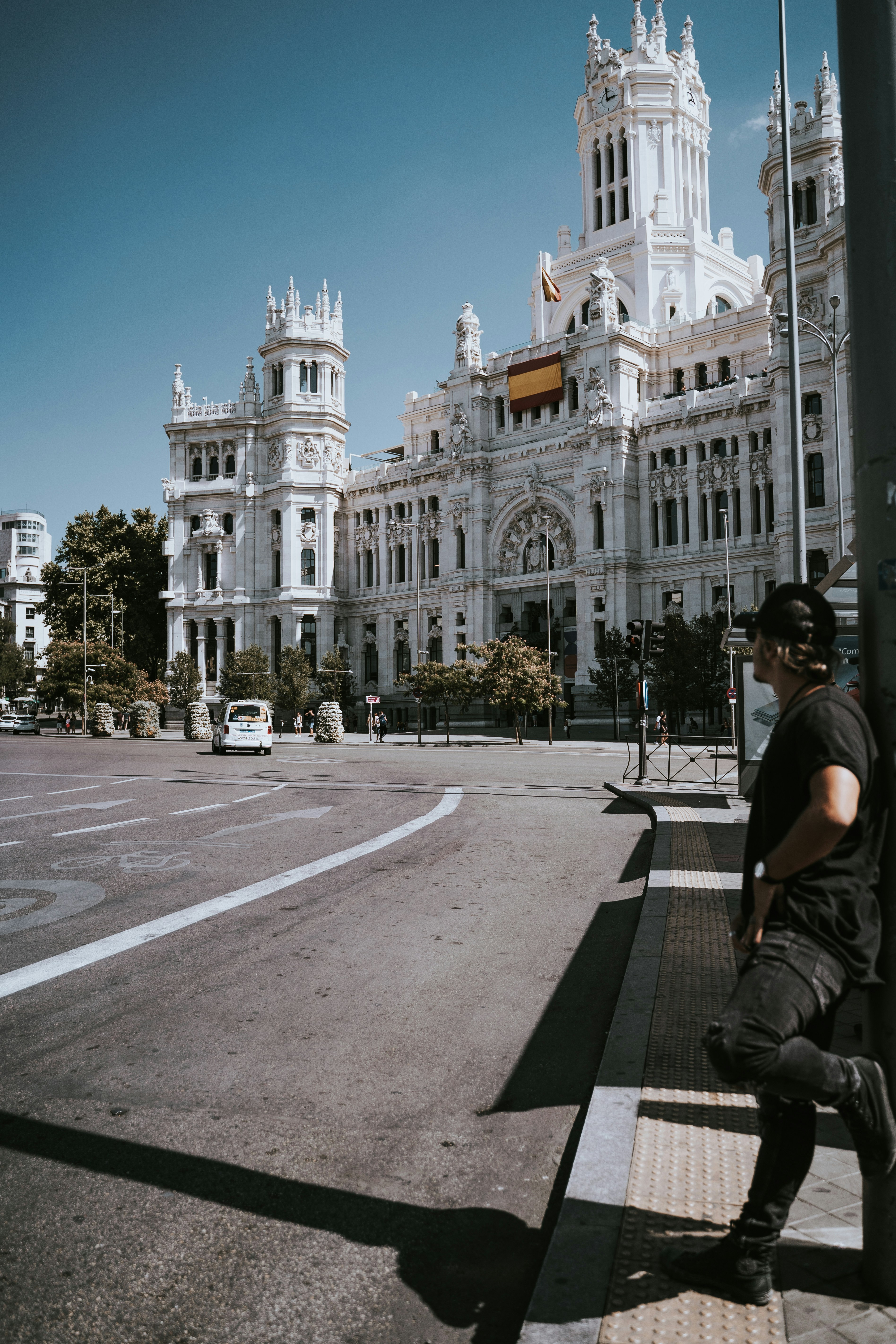 Man leans on pole in front of grand building.