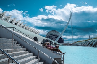 People relax by a futuristic building and water.