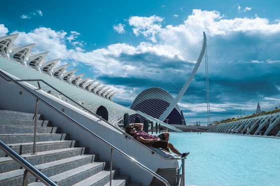 People relax by a futuristic building and water.