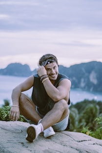 Man smiles while sitting on a rock overlooking the ocean.