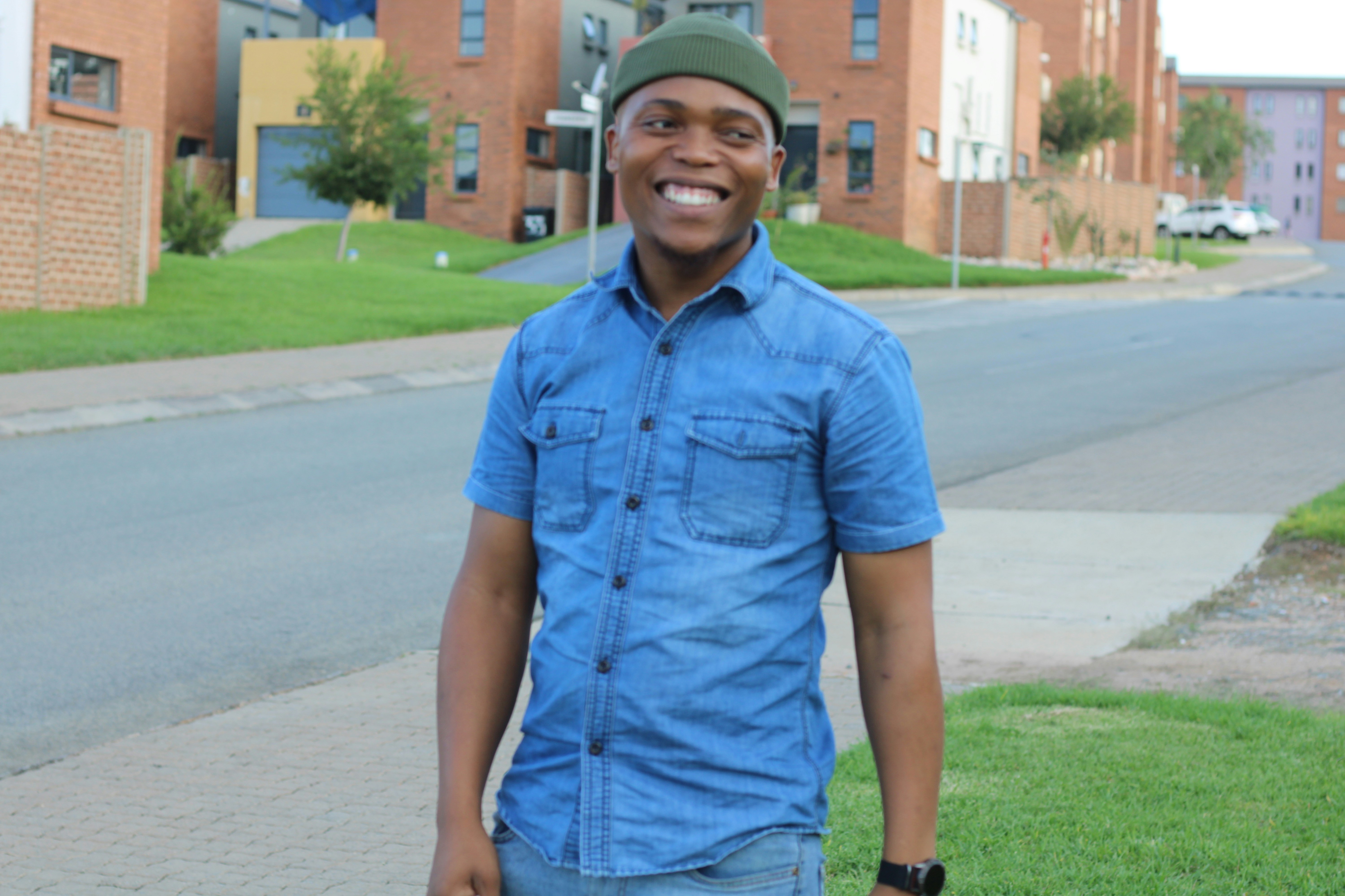 Smiling man stands on a sidewalk in front of buildings.