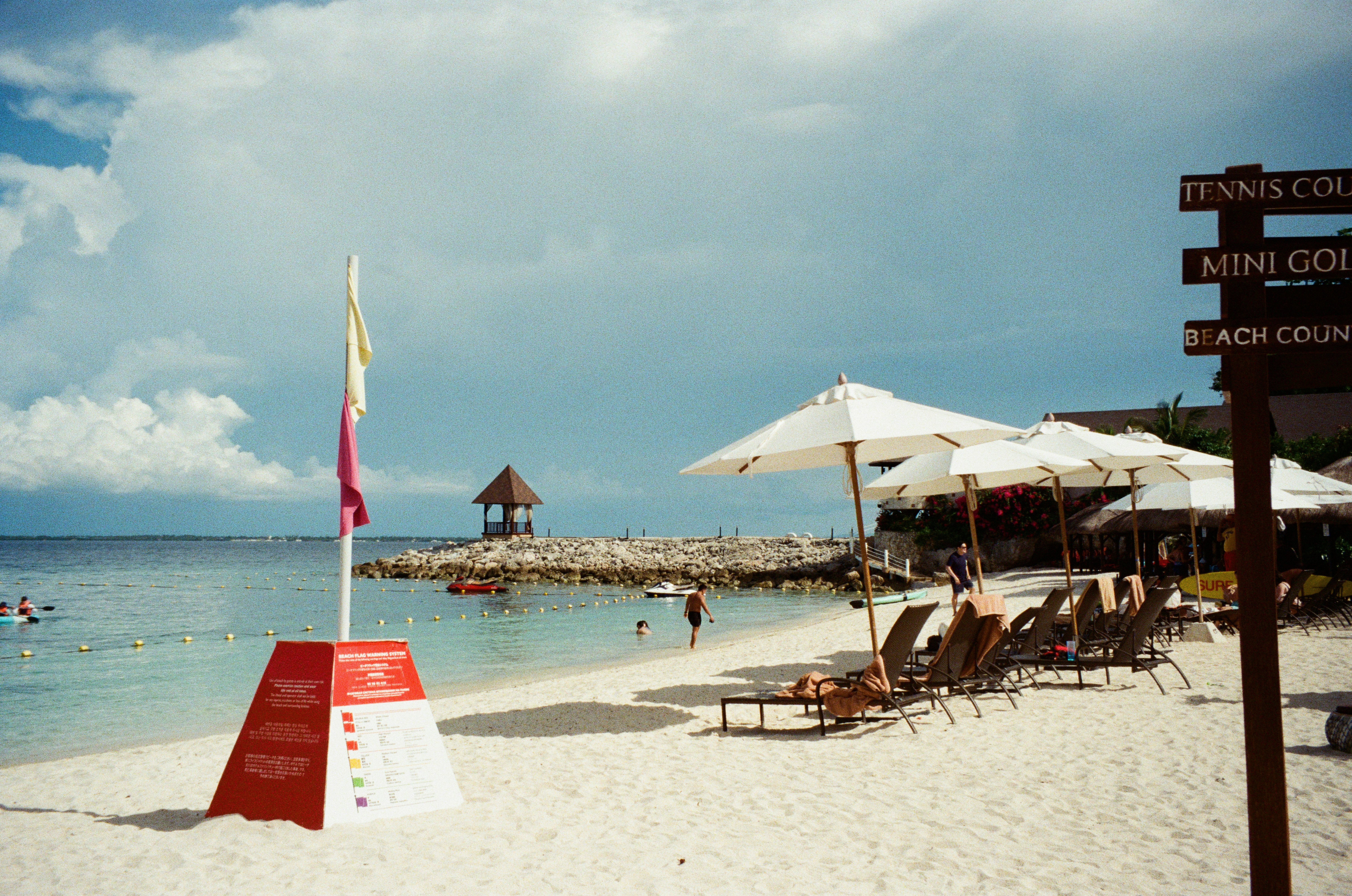 Beach scene with umbrellas, chairs, and a cloudy sky.