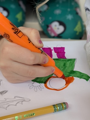 A child colors a picture with an orange marker.