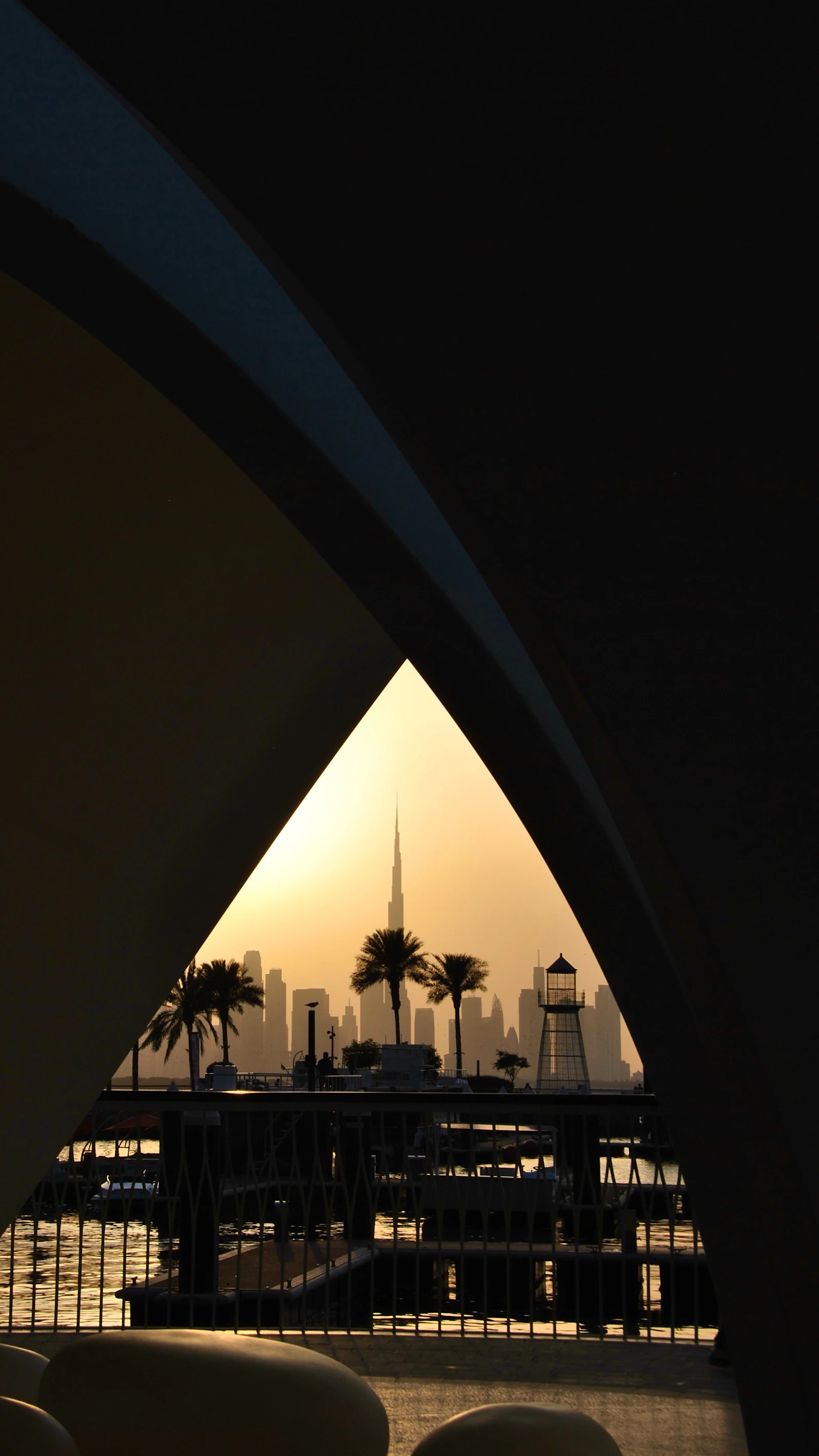 Travel photograph: Burj Khalifa and the Dubai skyline appear in the distance through a dark Creek-side arch at sunset.