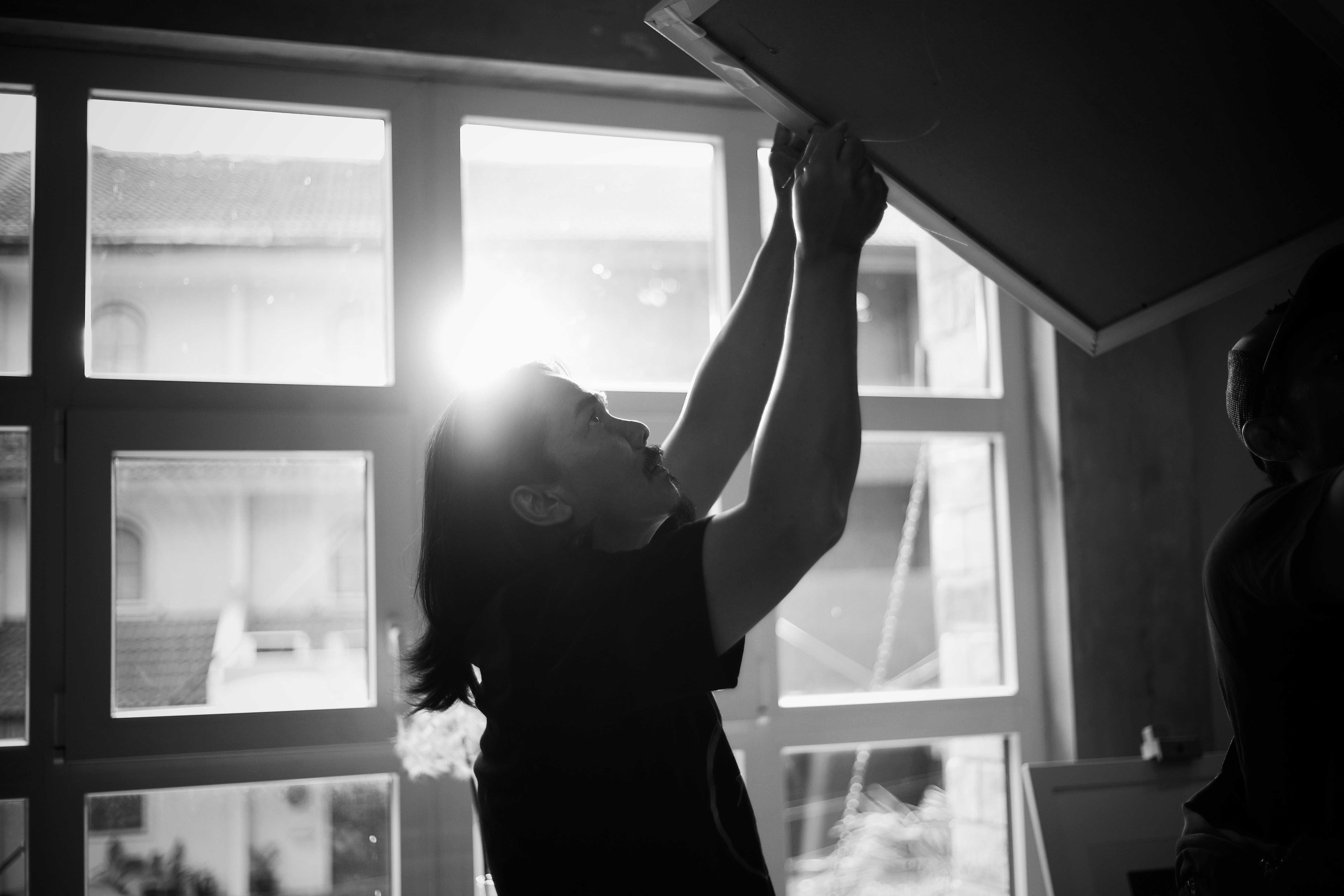 Silhouette of a person hanging curtains by a bright window