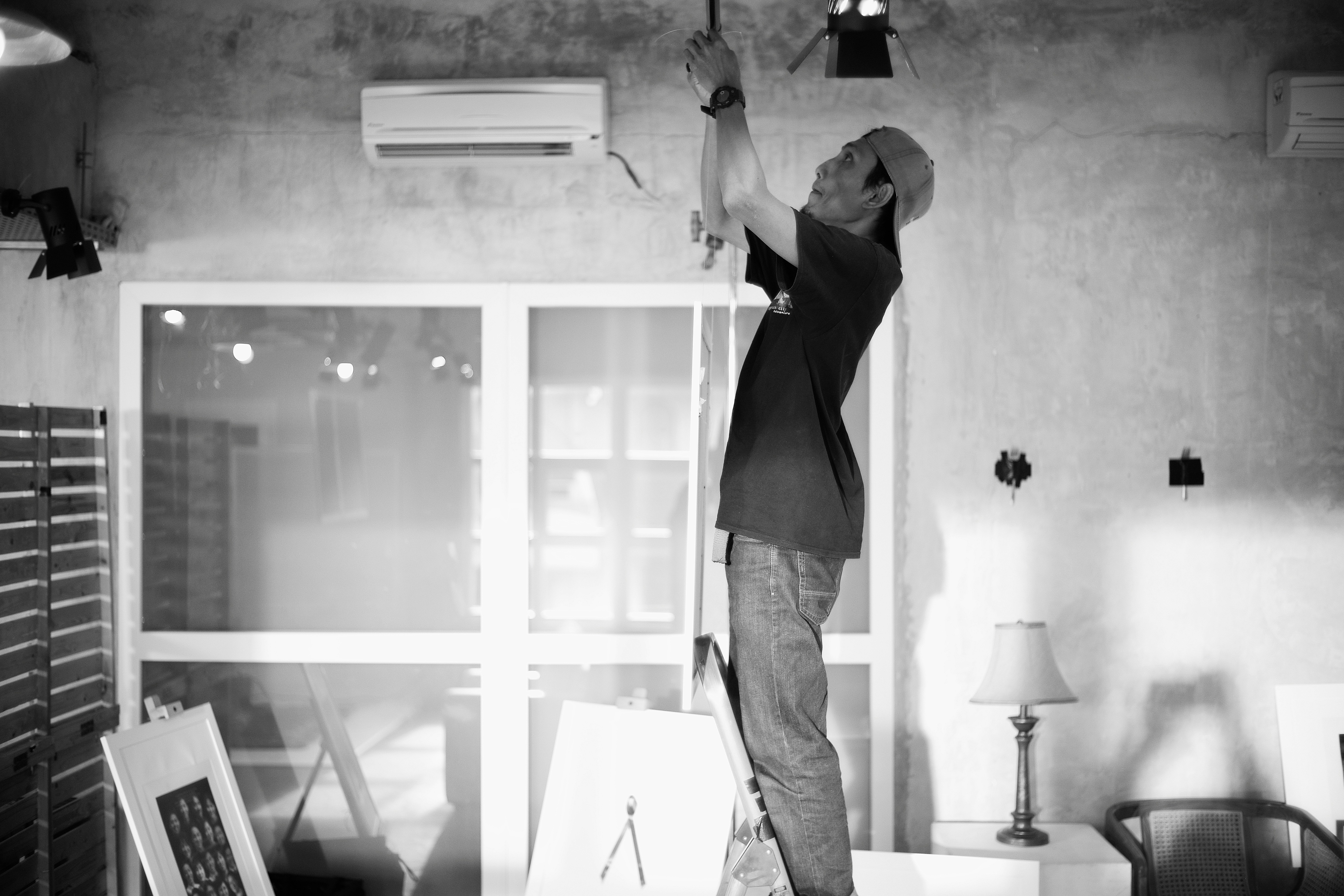 Electrician works on wiring from a ladder indoors.
