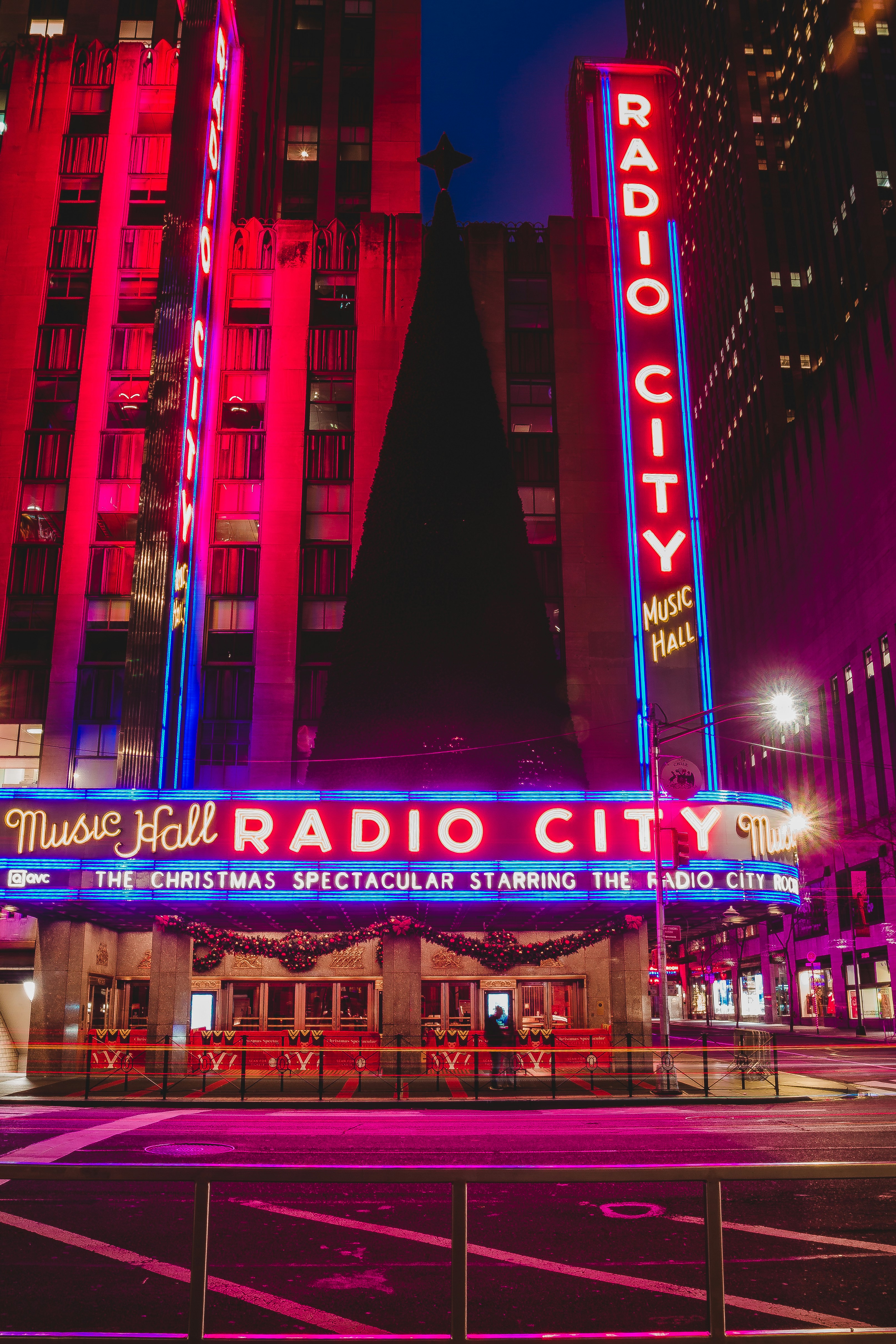 Radio city music hall is lit up at night.