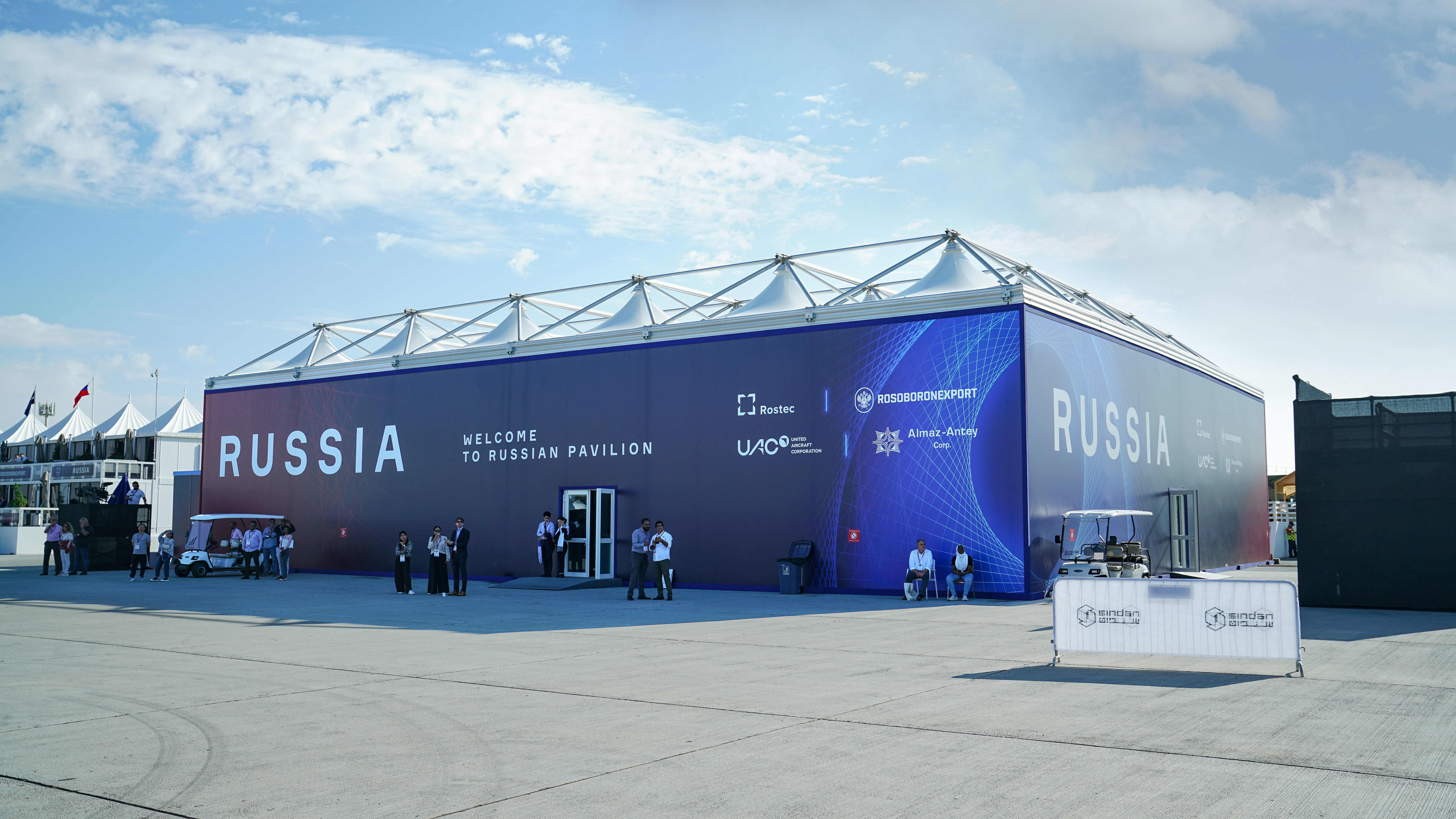 Business professionals network outside a large outdoor event pavilion.