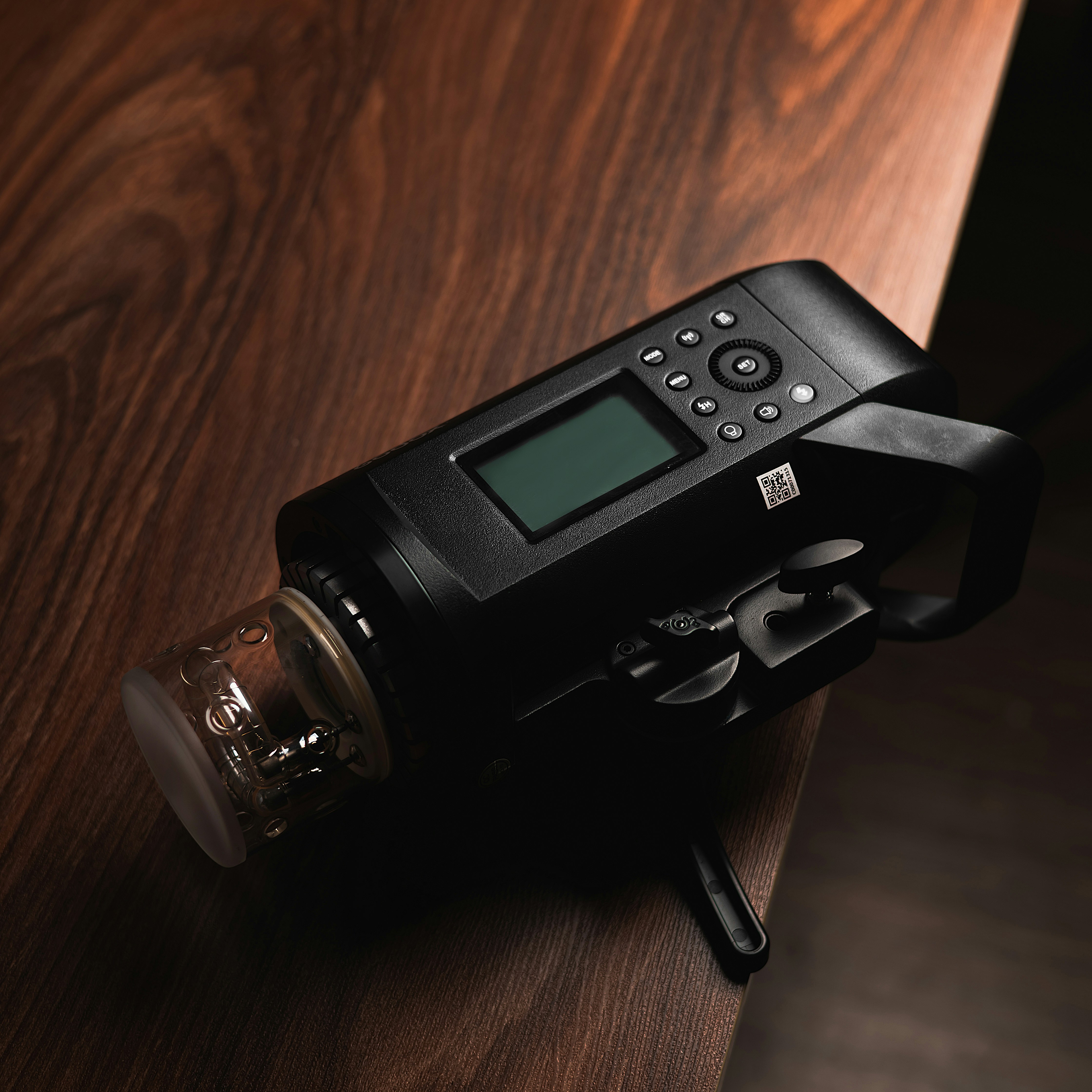 A photography flash lies on a wooden table.