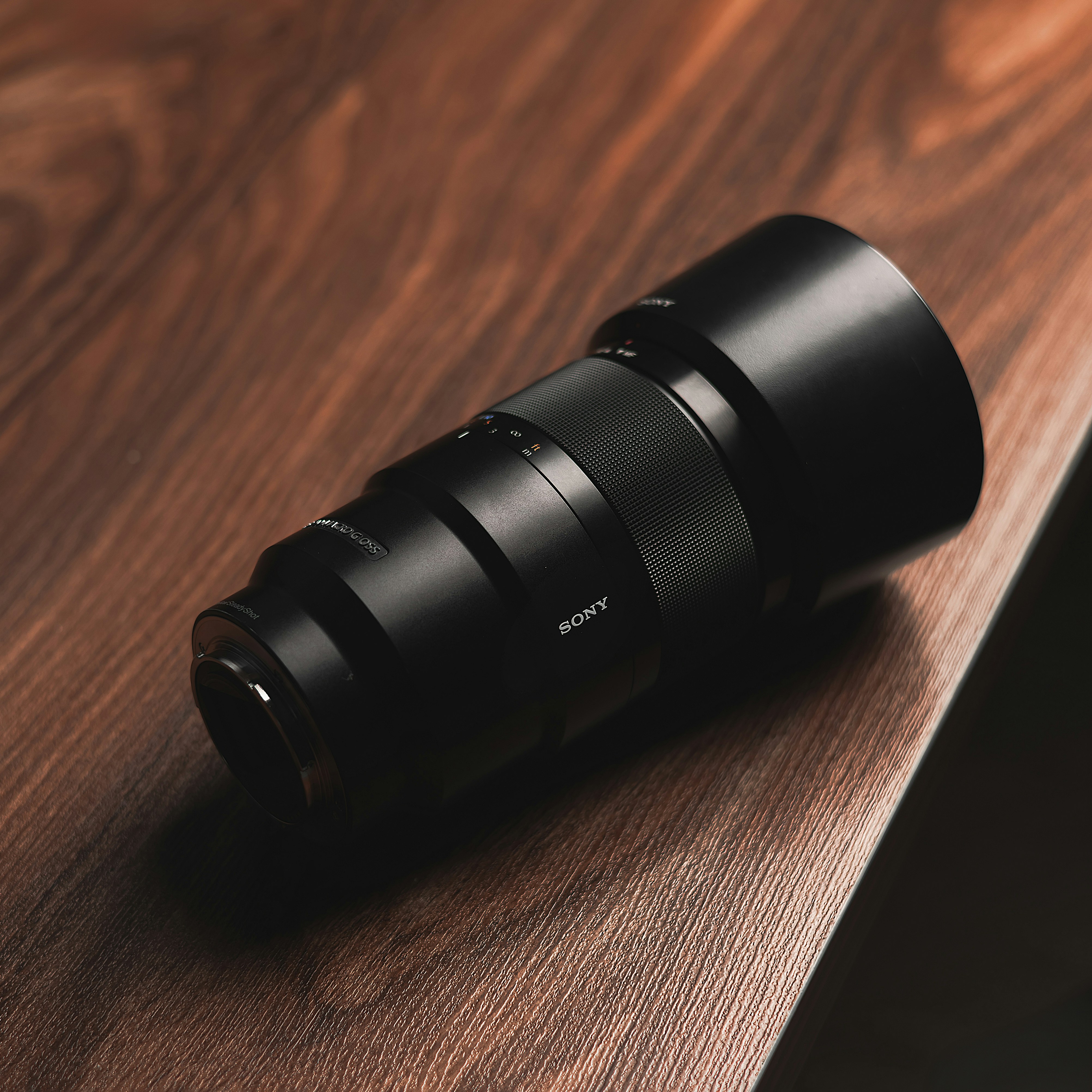 A sony camera lens rests on wood.