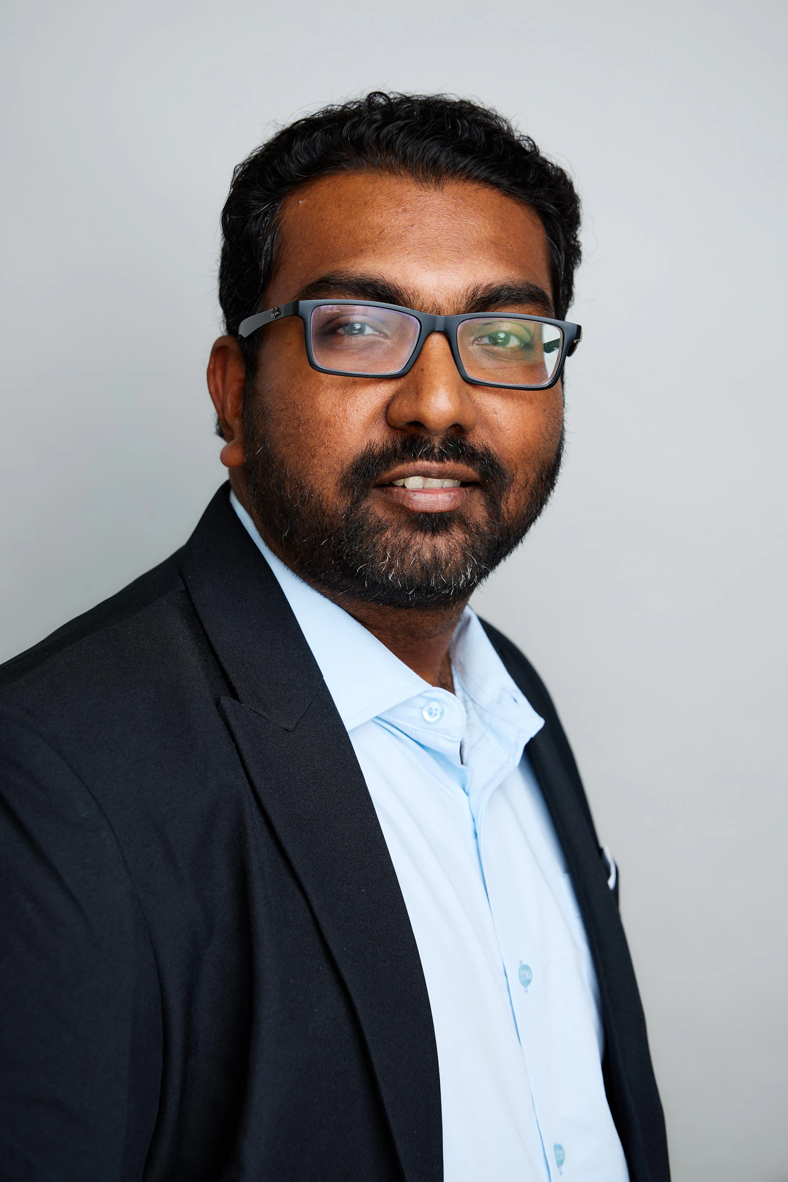 A confident Indian business owner in a dark suit and light blue shirt