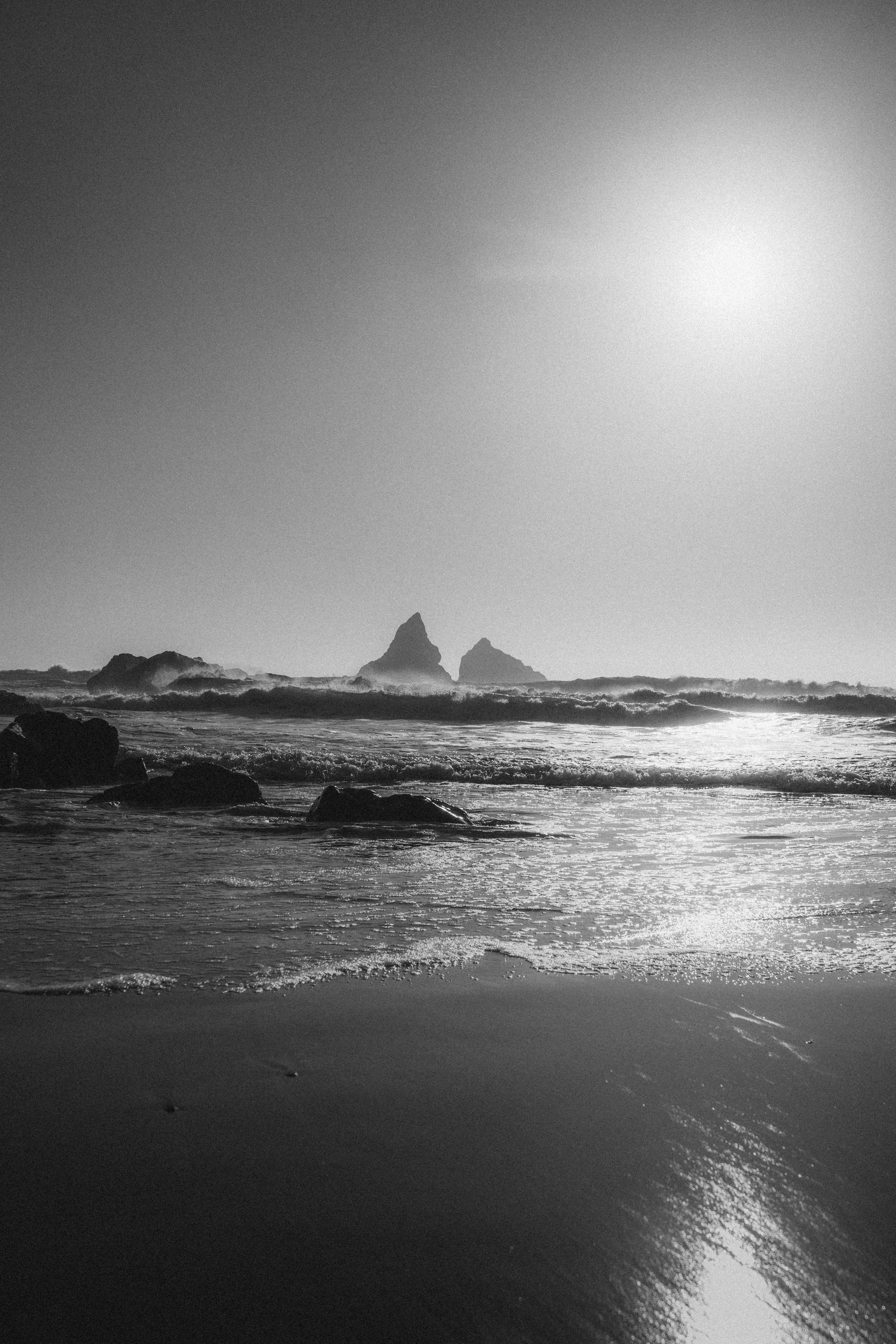 Waves crash against a rocky shore under the sun.