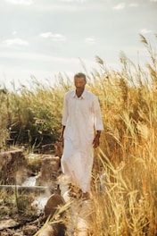 Man walks through tall grass near a water source.