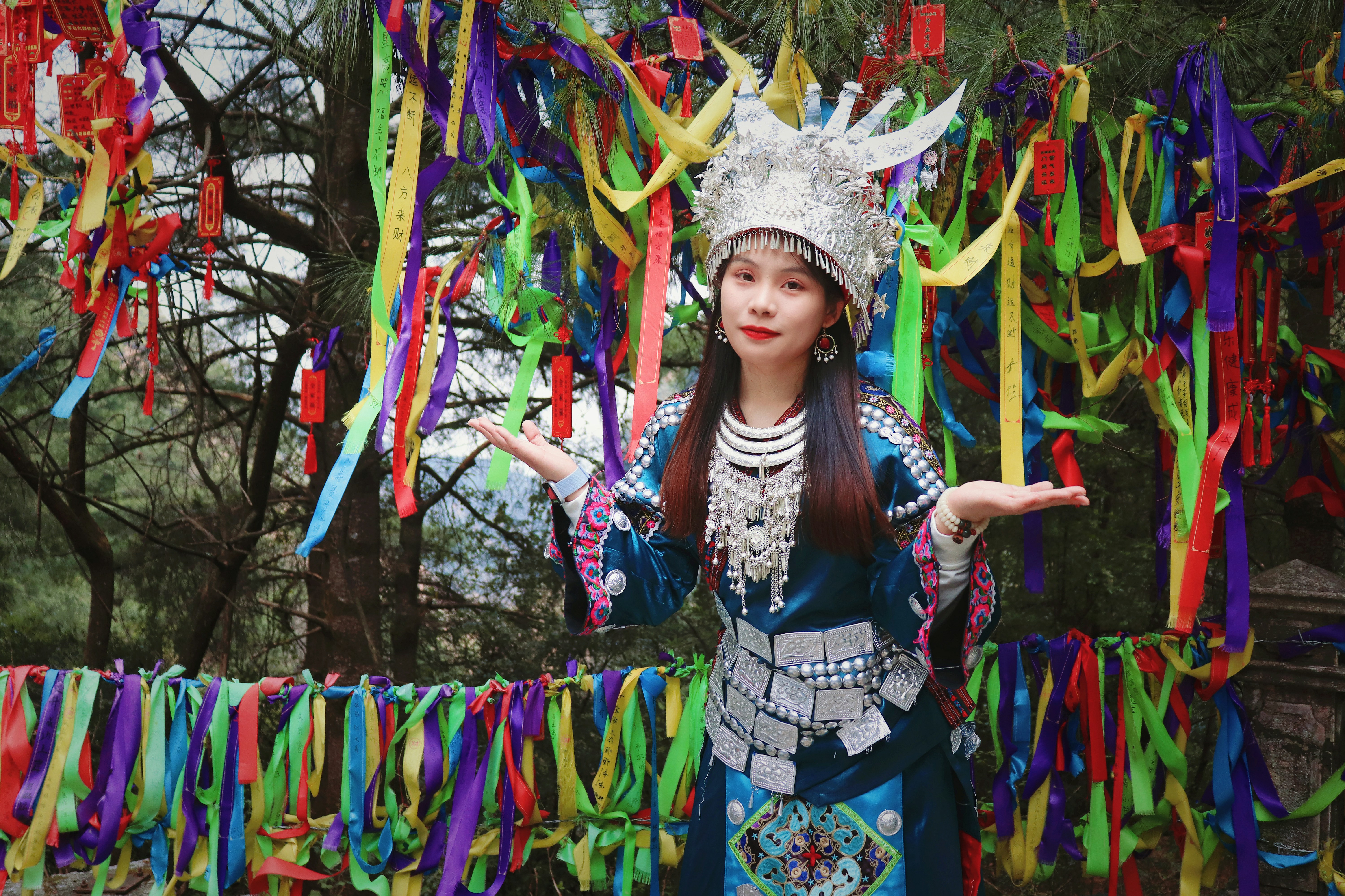 Woman in traditional dress stands by colorful ribbons.