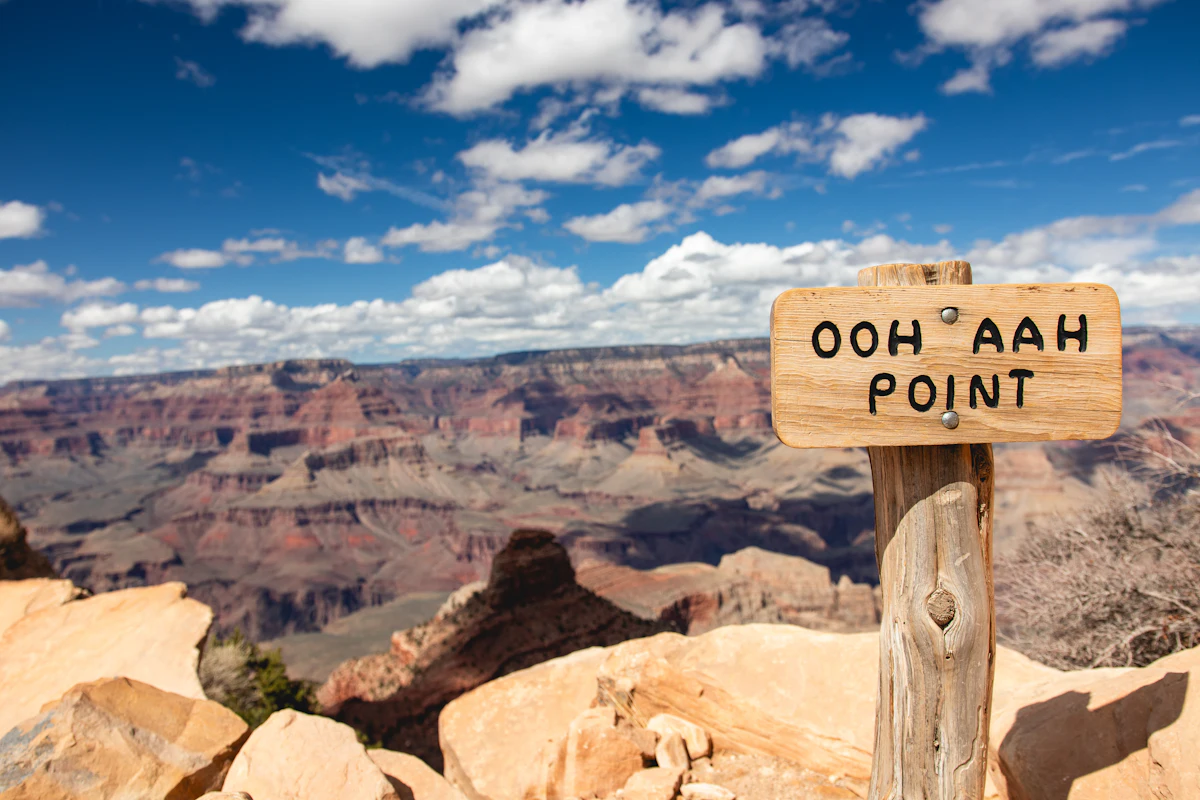 The Ooh Aah Point sign above the Grand Canyon, with red cliffs and buttes beyond