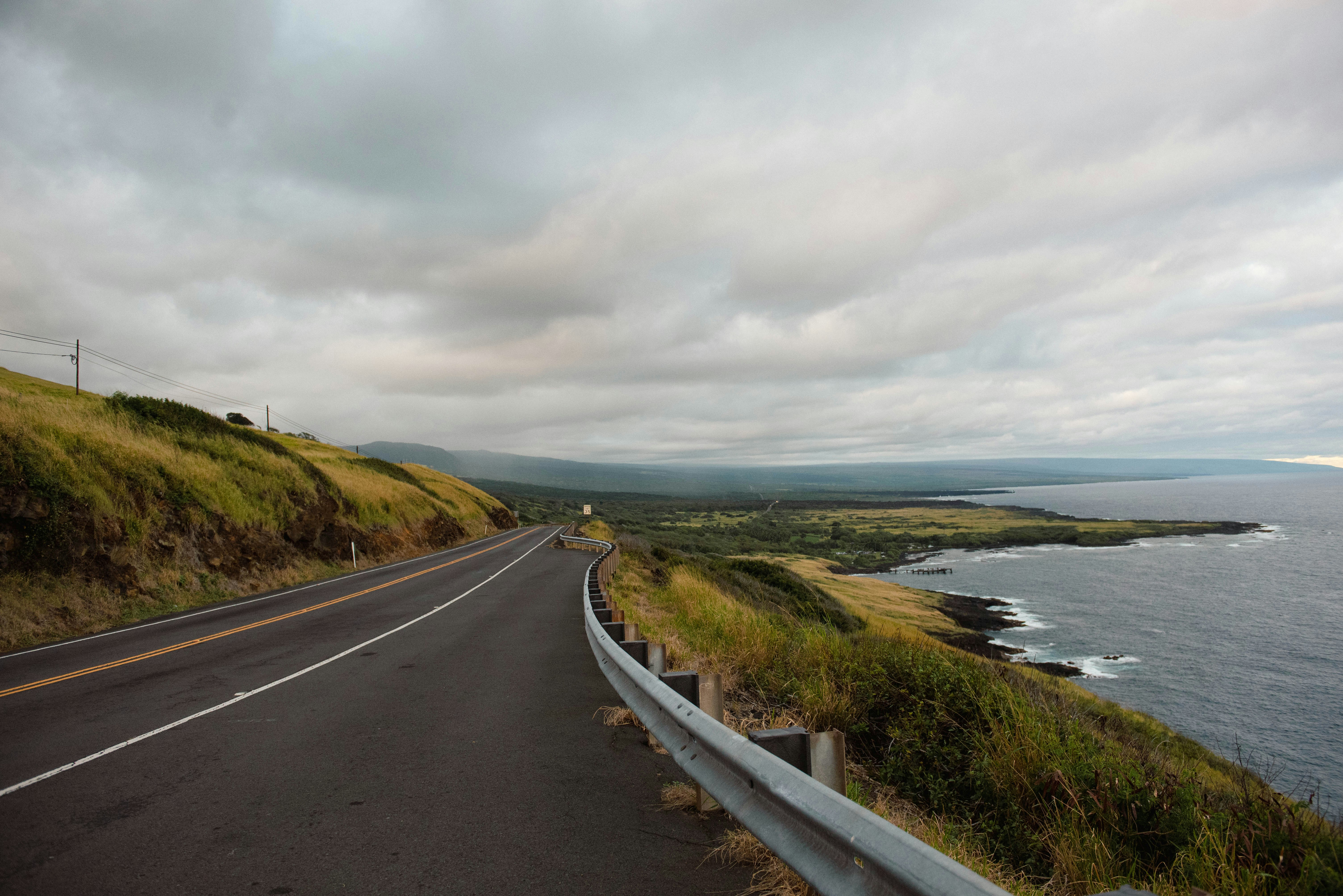 Road curves along coast under cloudy skies.
