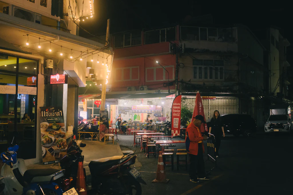 Bangkok street at night with open food shops, parked motorbikes and warm bulbs