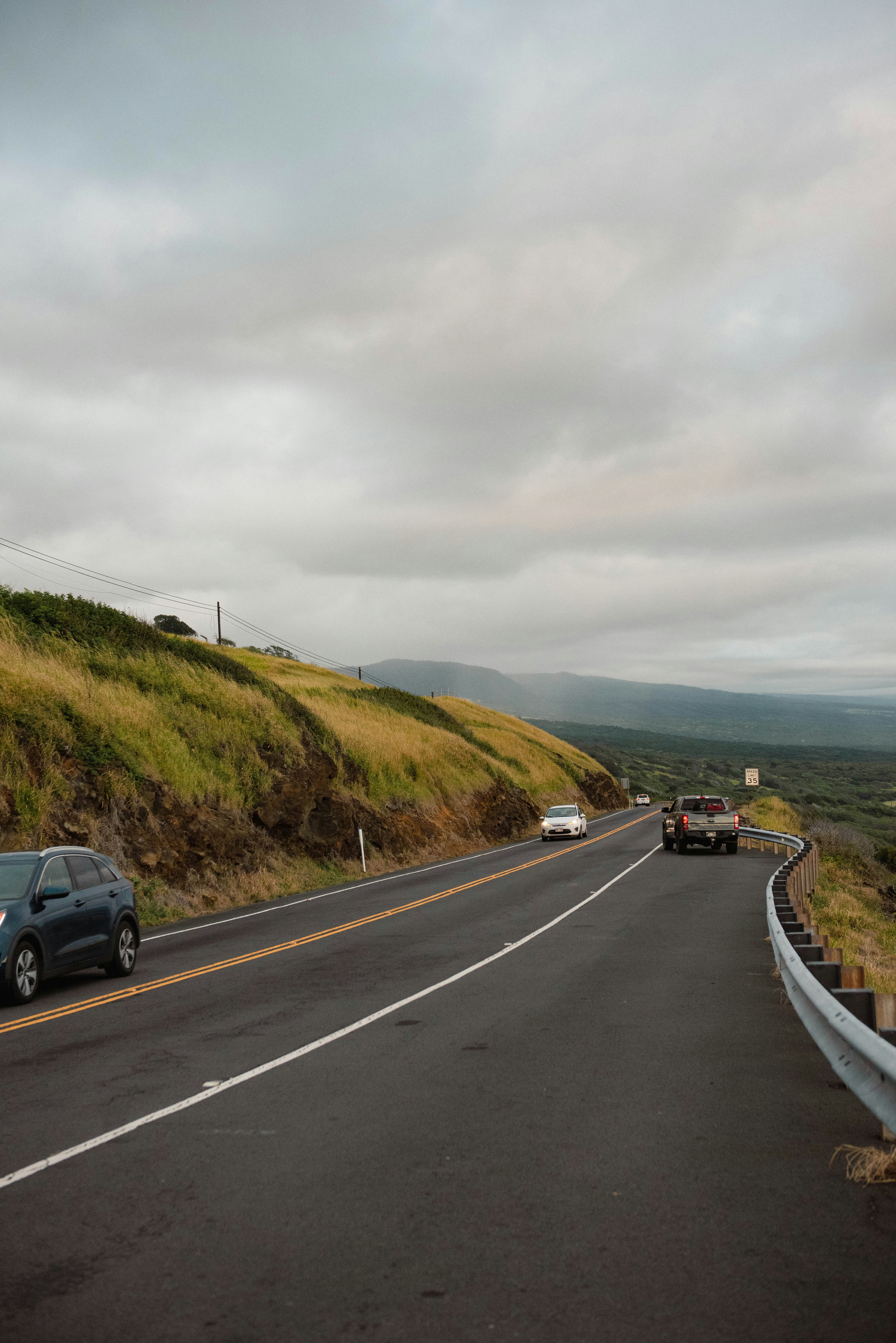 Cars drive on a winding road under cloudy skies.