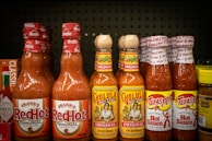Shelf displays various bottles of hot sauce.