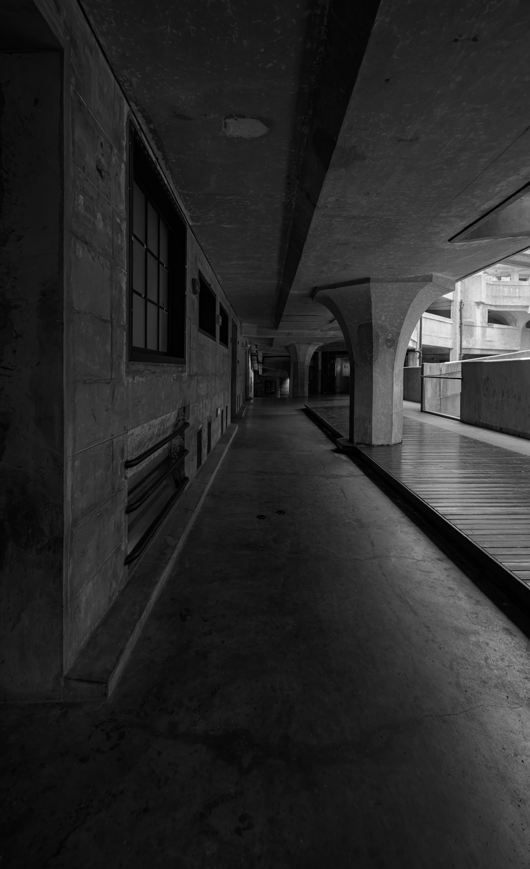A Dark Concrete Institutional Corridor Photographed In Black And White