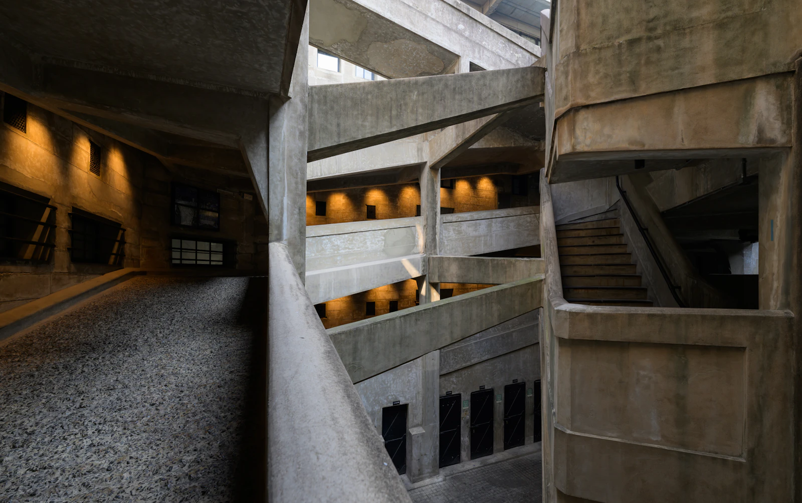 Interlocking concrete ramps and walkways inside a dark brutalist building, lit by warm golden recessed lights