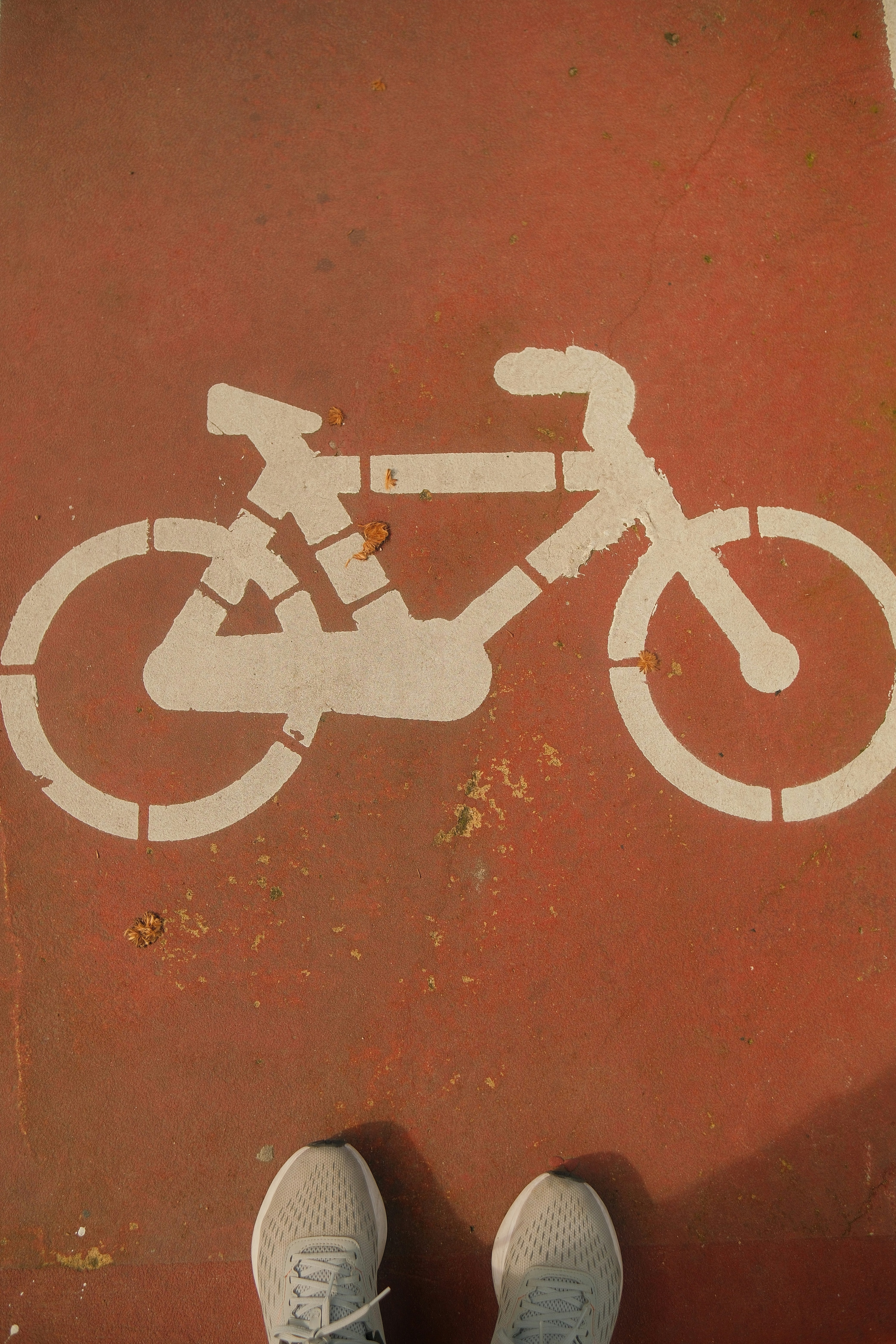 Bicycle lane symbol on red pavement with feet.