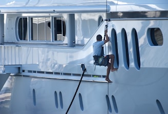 A man is climbing the side of a yacht.