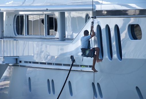 A man is climbing the side of a yacht.