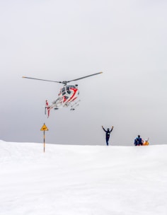 Helicopter arrives to help people on snowy terrain.
