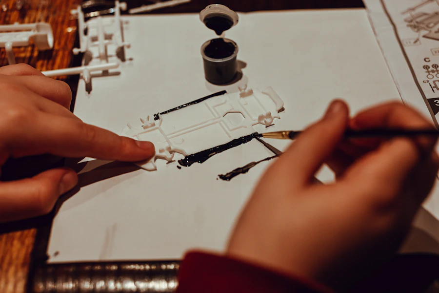 Hands painting small figure parts with a fine brush, pots of paint open on the bench