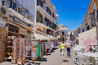 A sunny street lined with shops and people.