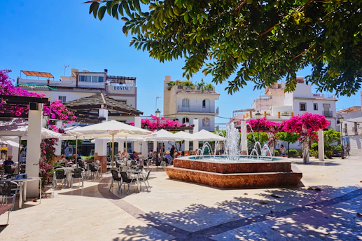 A sunny plaza features a fountain and outdoor cafe.