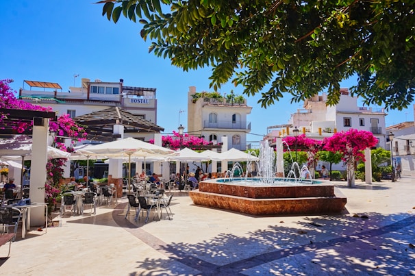 A sunny plaza features a fountain and outdoor cafe.