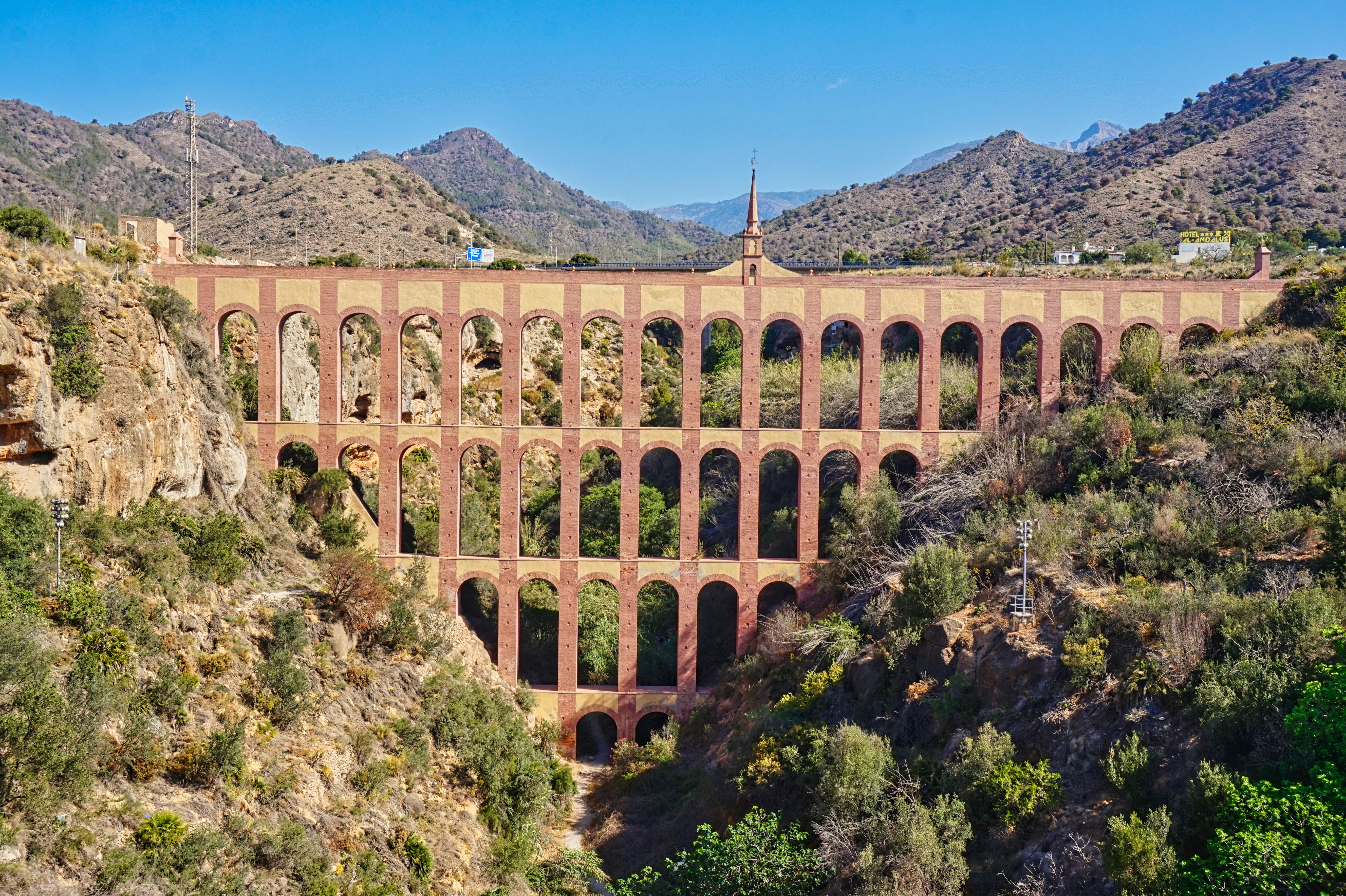Ein gewölbtes Aquädukt erstreckt sich über eine bergige Landschaft.