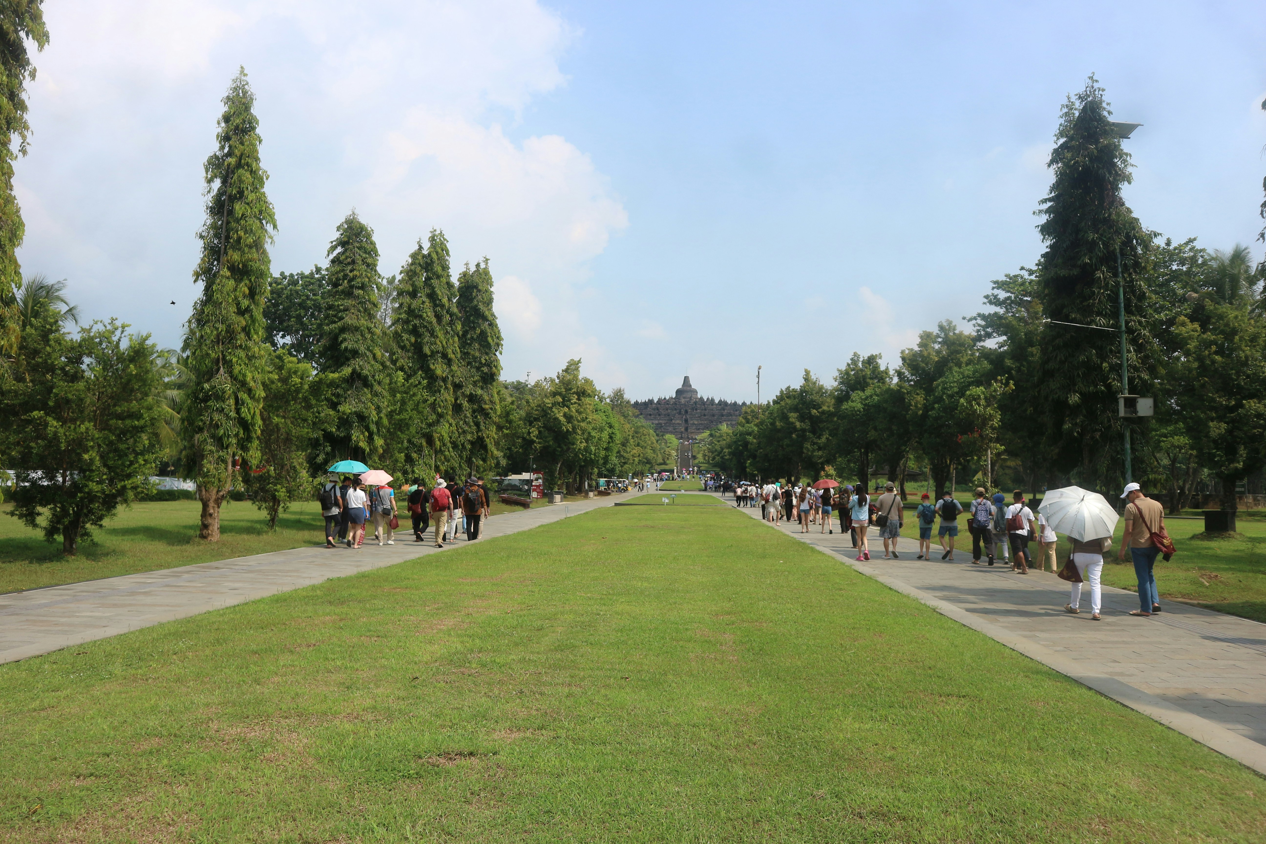 People walk down a long grassy path.