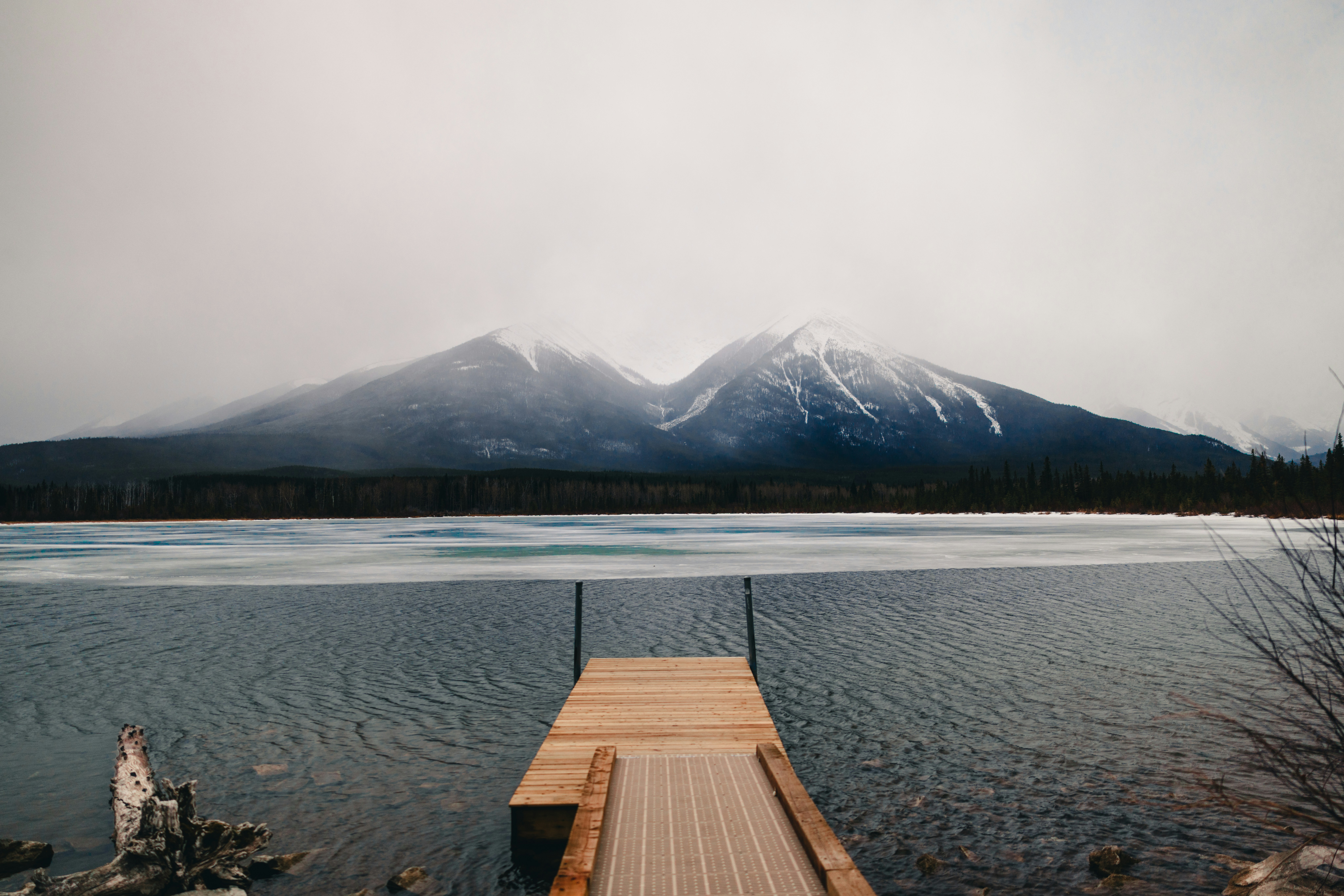 Pier faces snowy mountains across a lake.