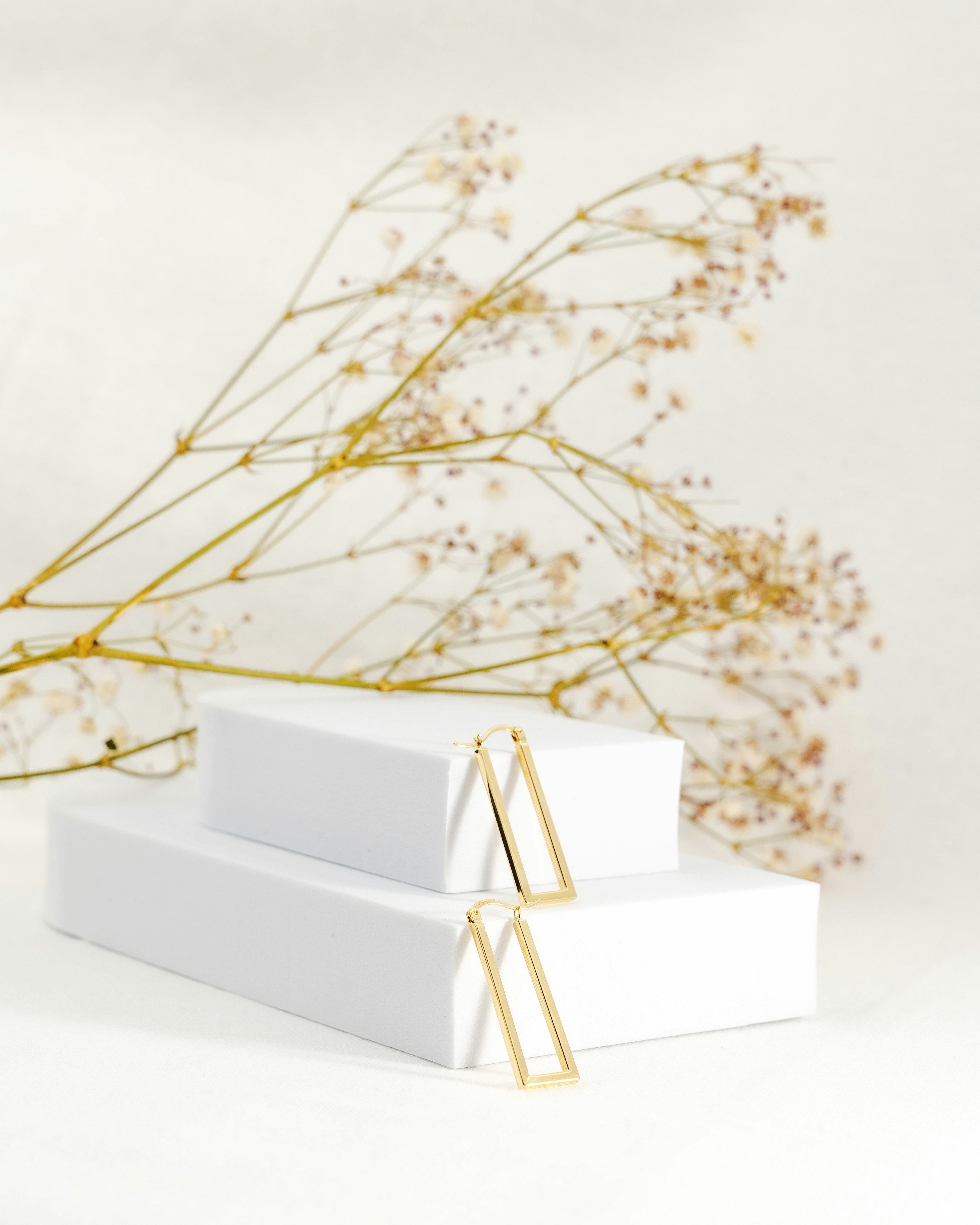 Elegant golden earrings displayed with dried flowers.