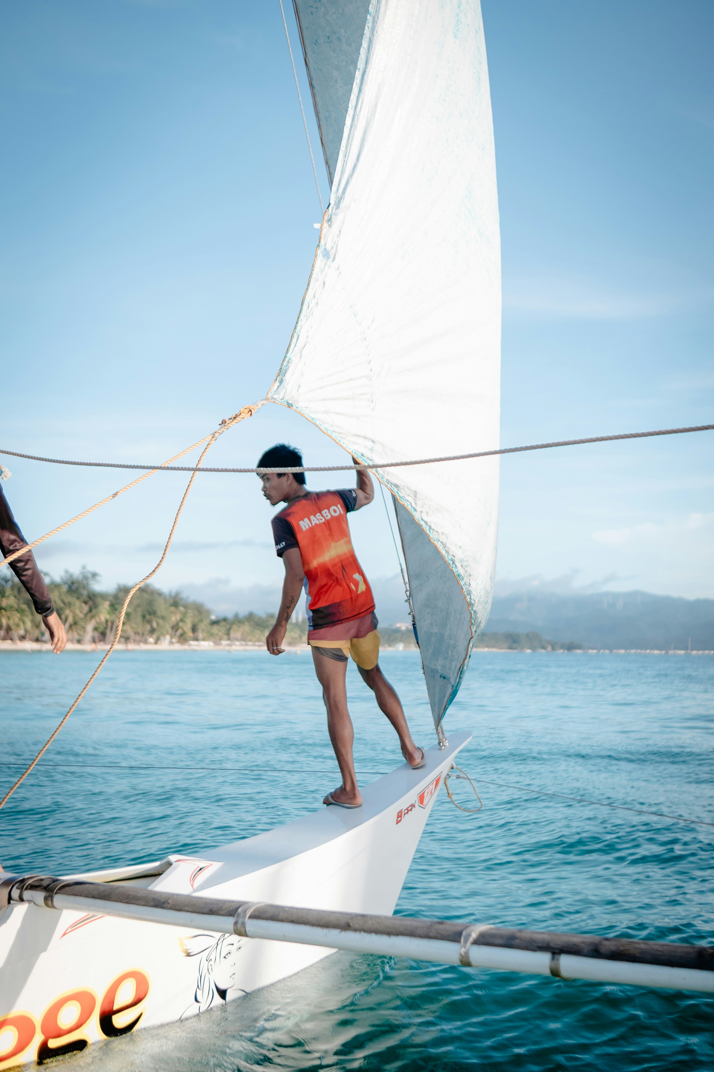 Man adjusts sail on a boat in ocean.