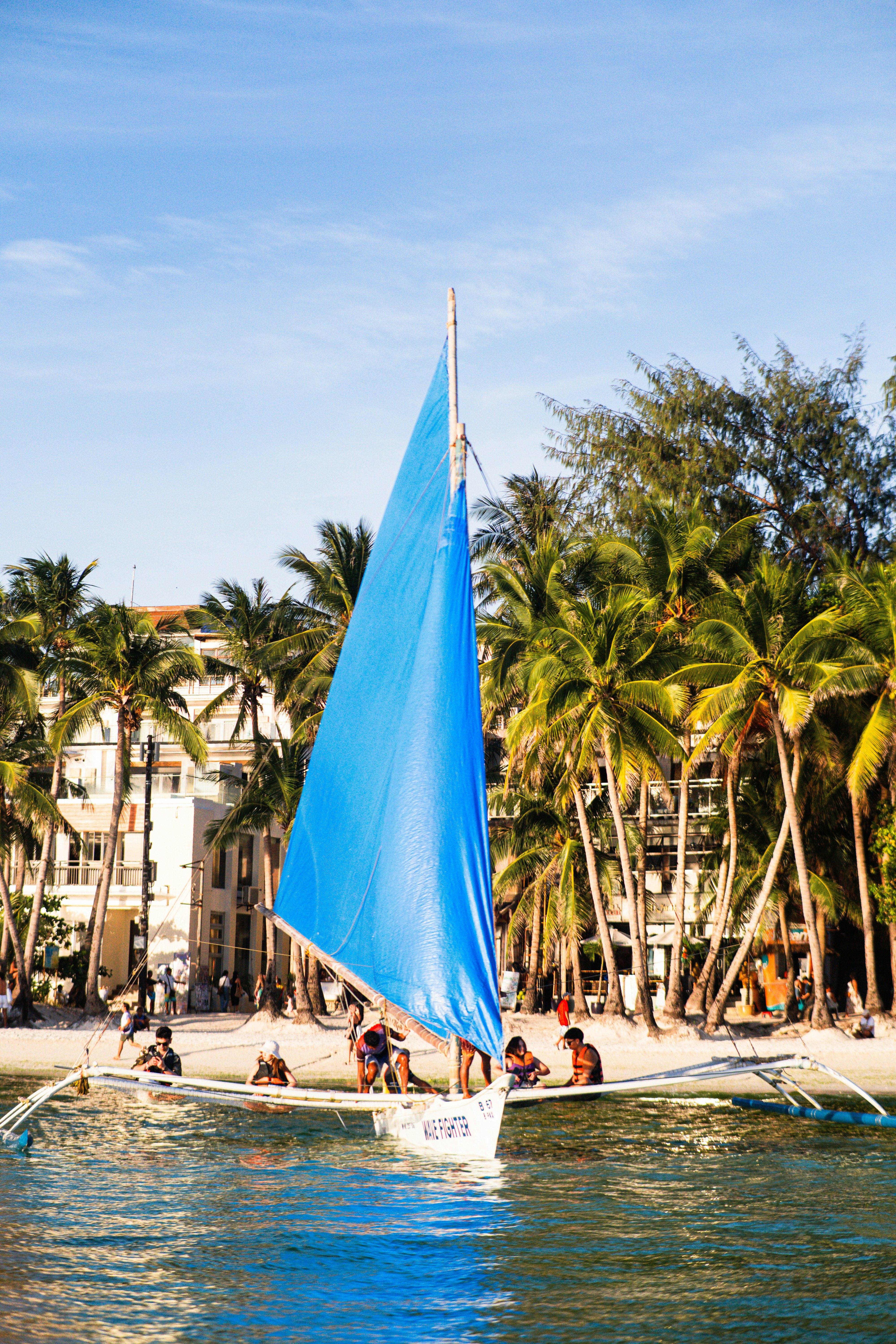 A sailboat with a blue sail near palm trees.