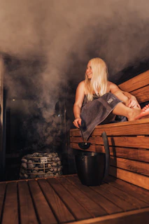 Woman relaxes and pours water in a hot sauna.