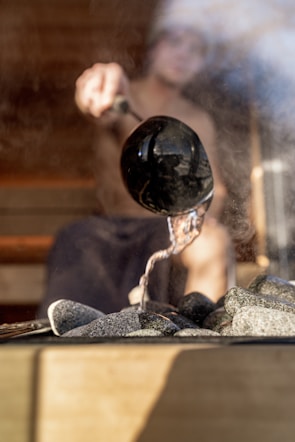 A man pours water on hot sauna rocks.