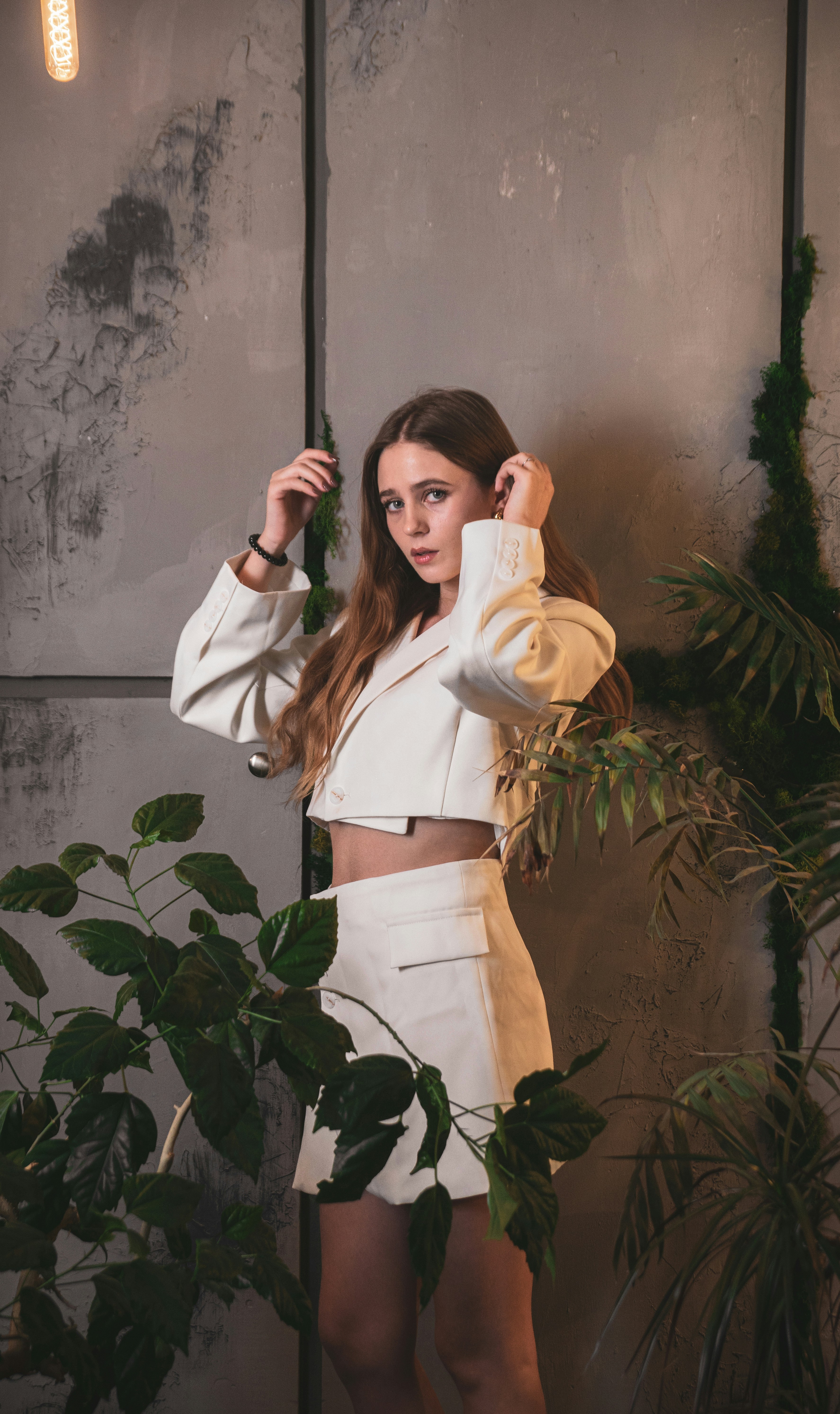A woman in a white suit poses among plants.
