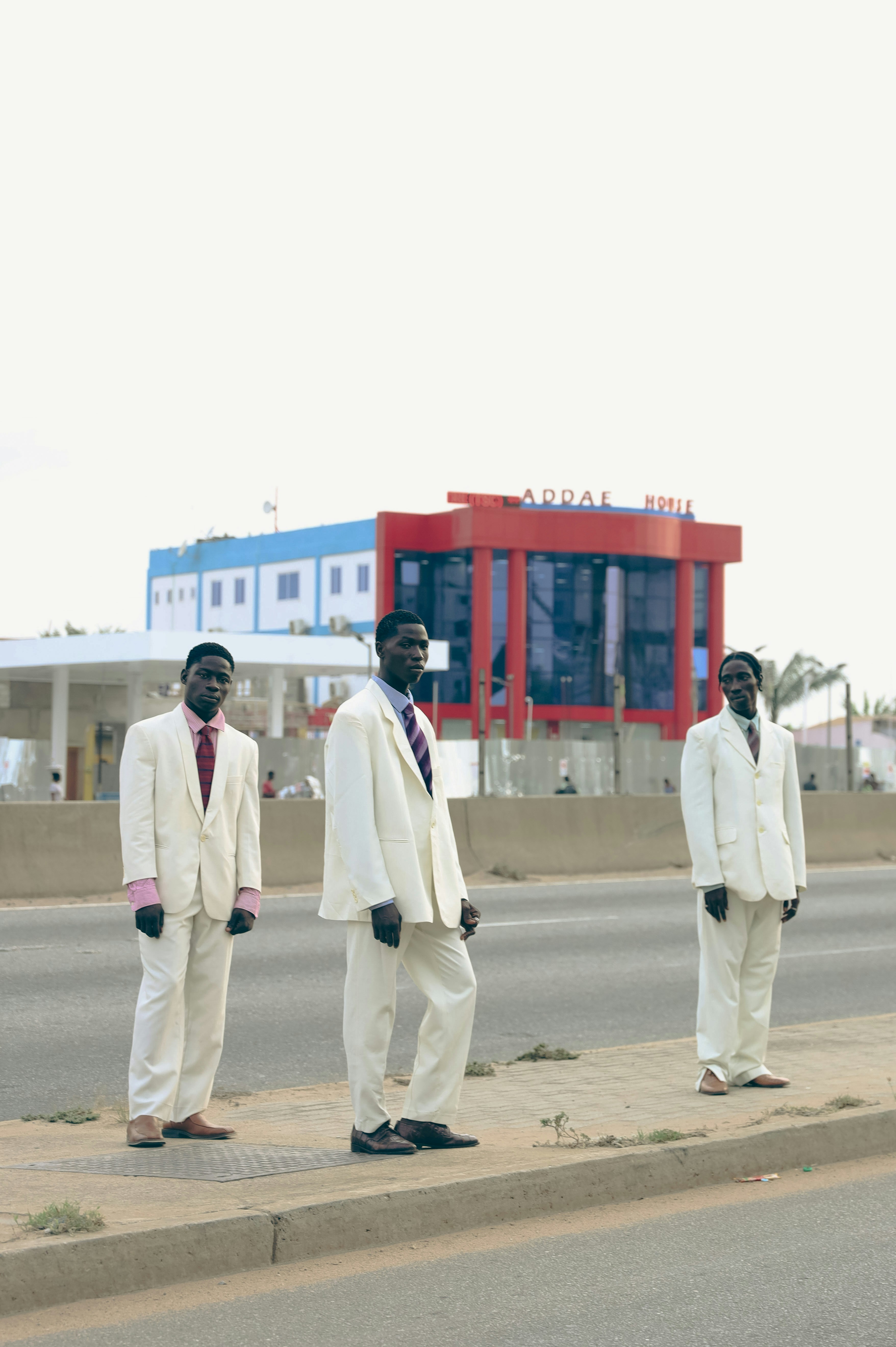 Three men stand on a sidewalk in suits.