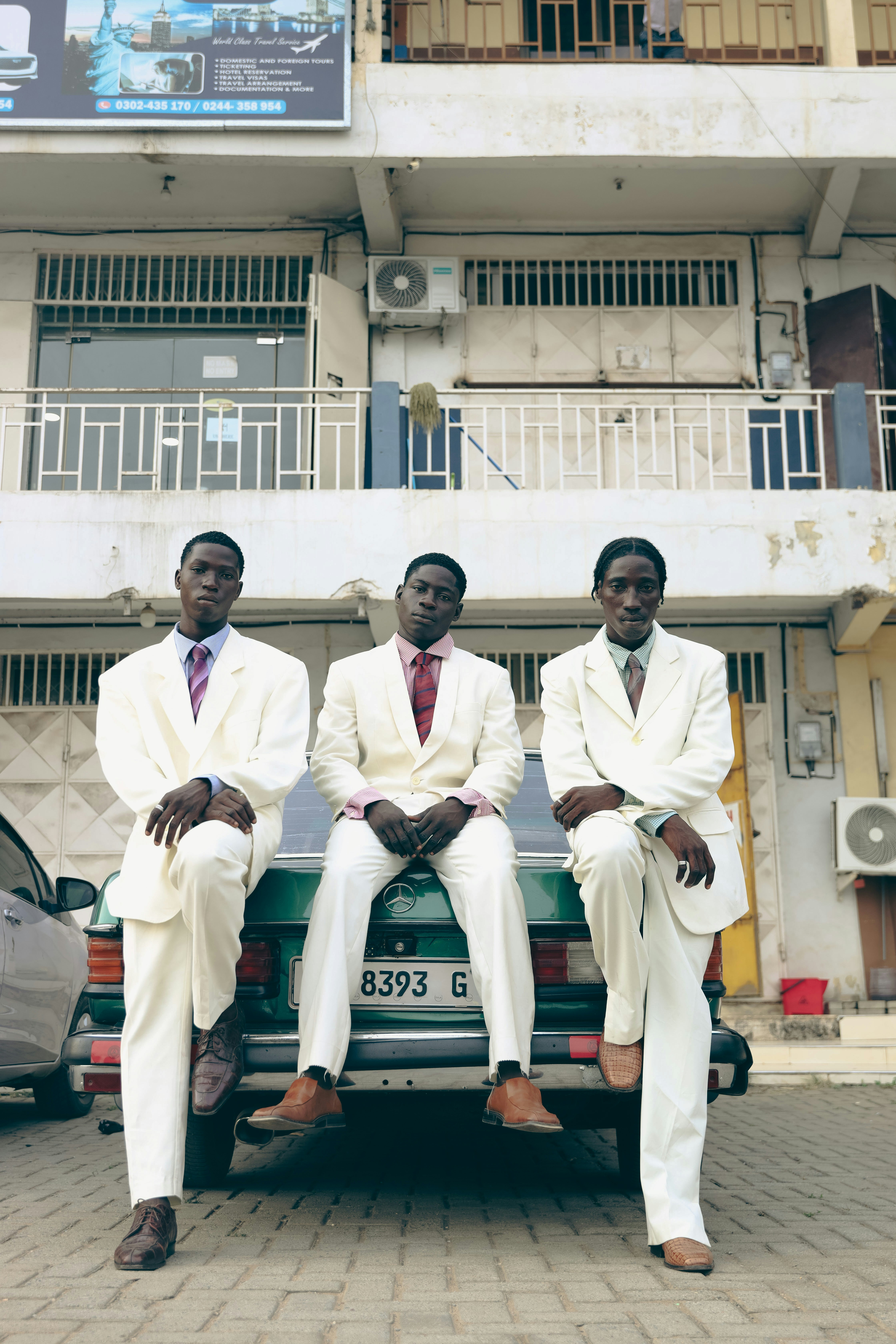 Three men in white suits pose in front of a building.