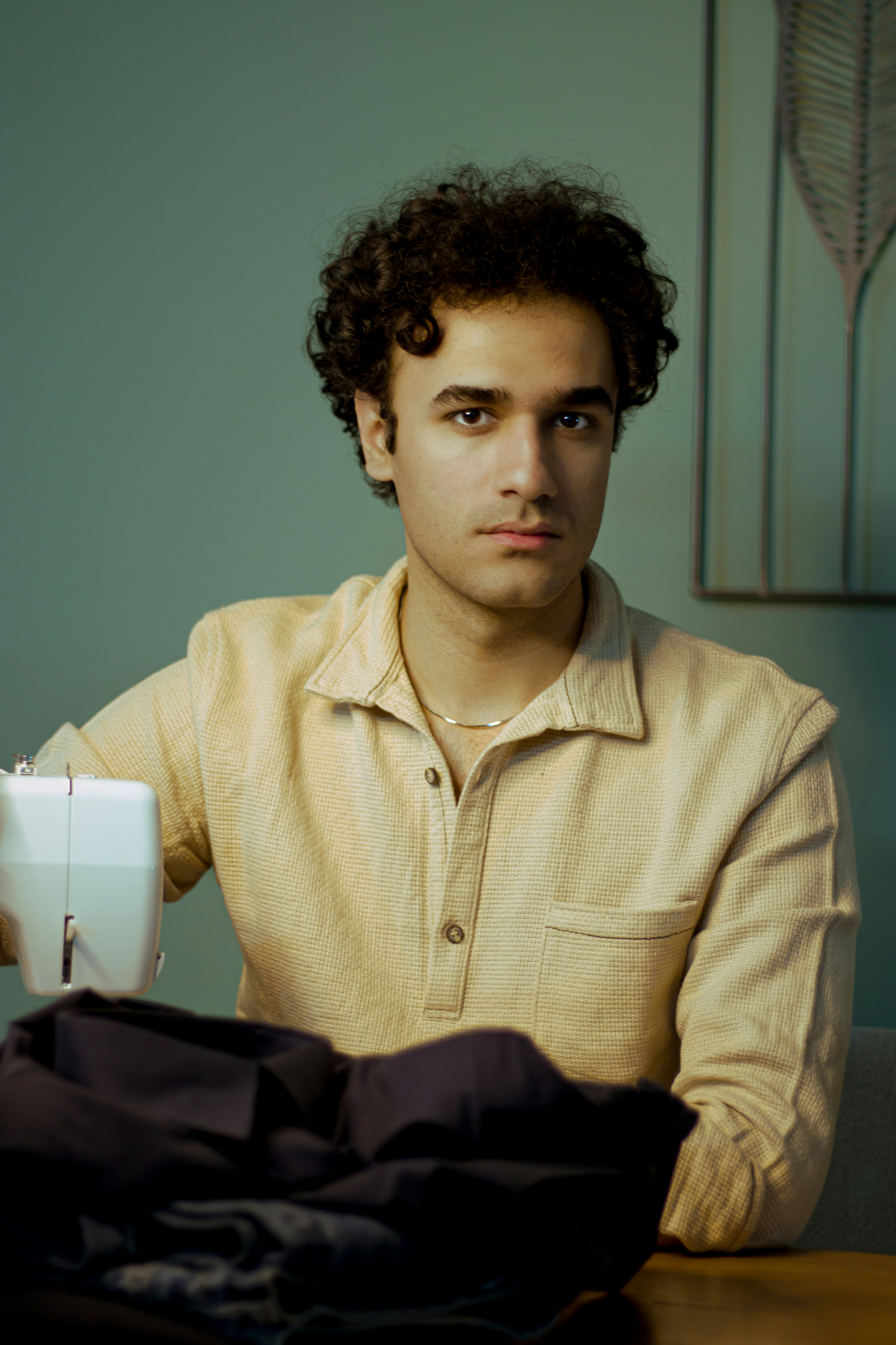 Junger Mann sitzt mit Nähmaschine.