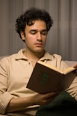 Man with curly hair is reading a book.