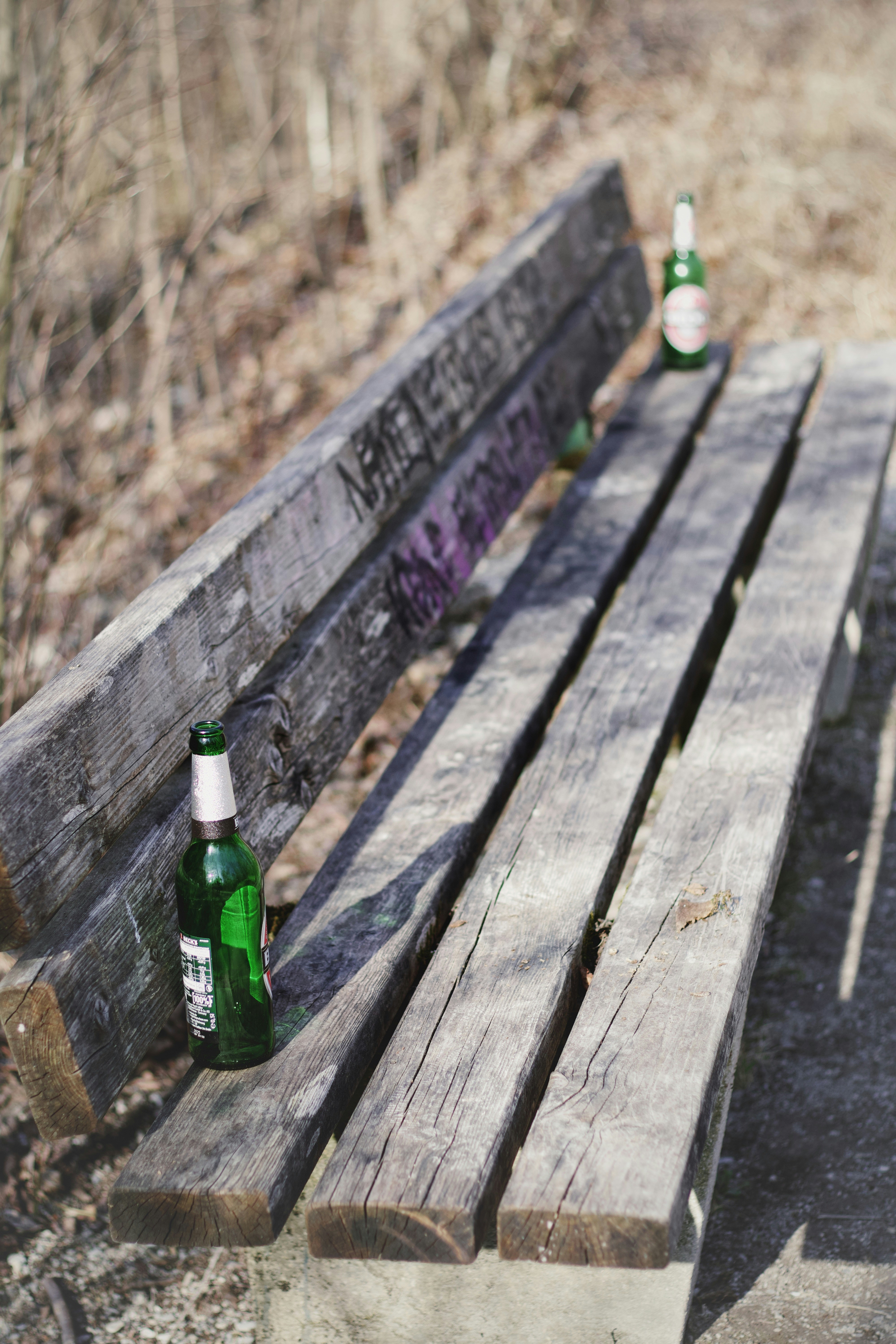 Beer bottles sit on a weathered park bench.