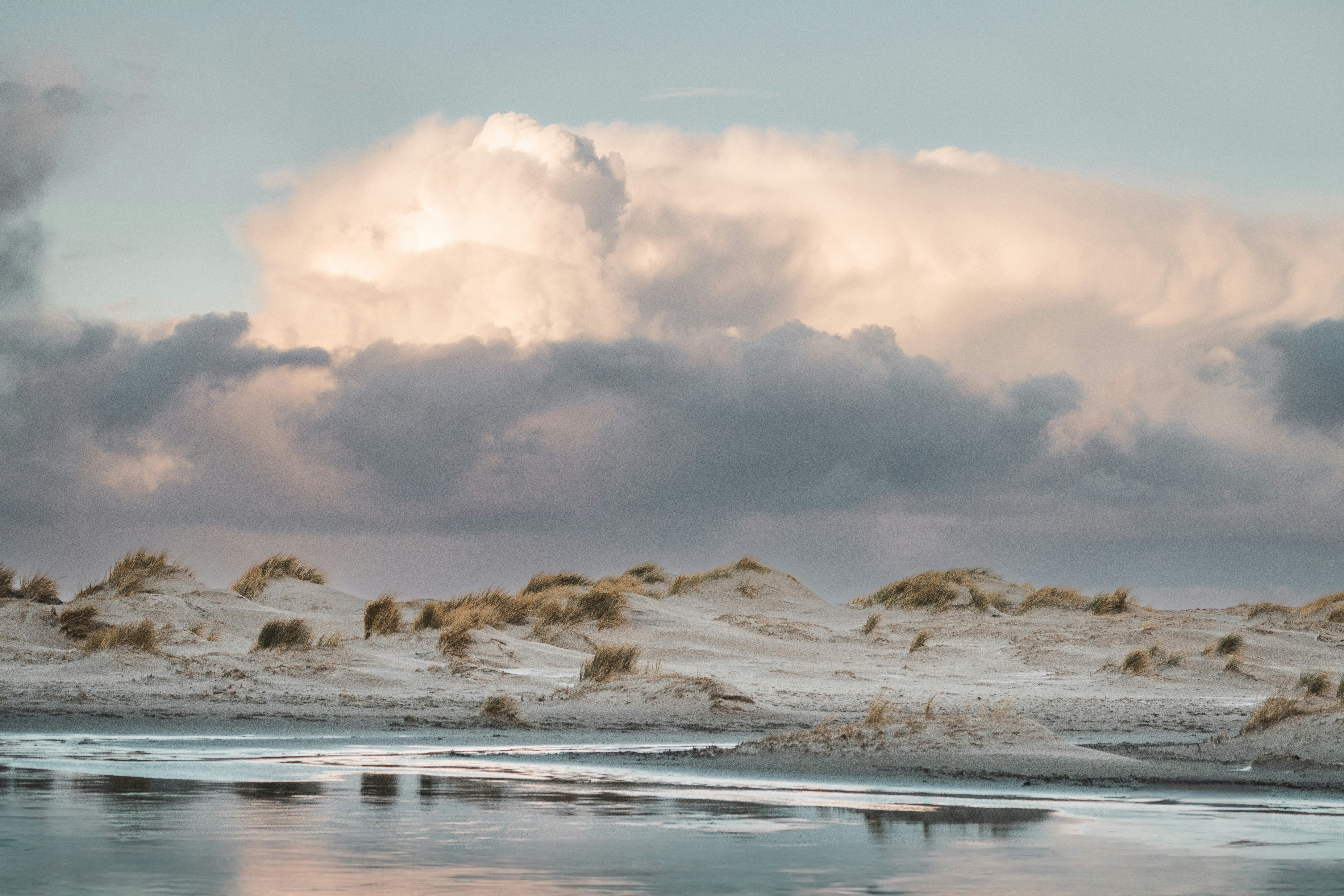 Cloudy sky above sandy dunes and water.