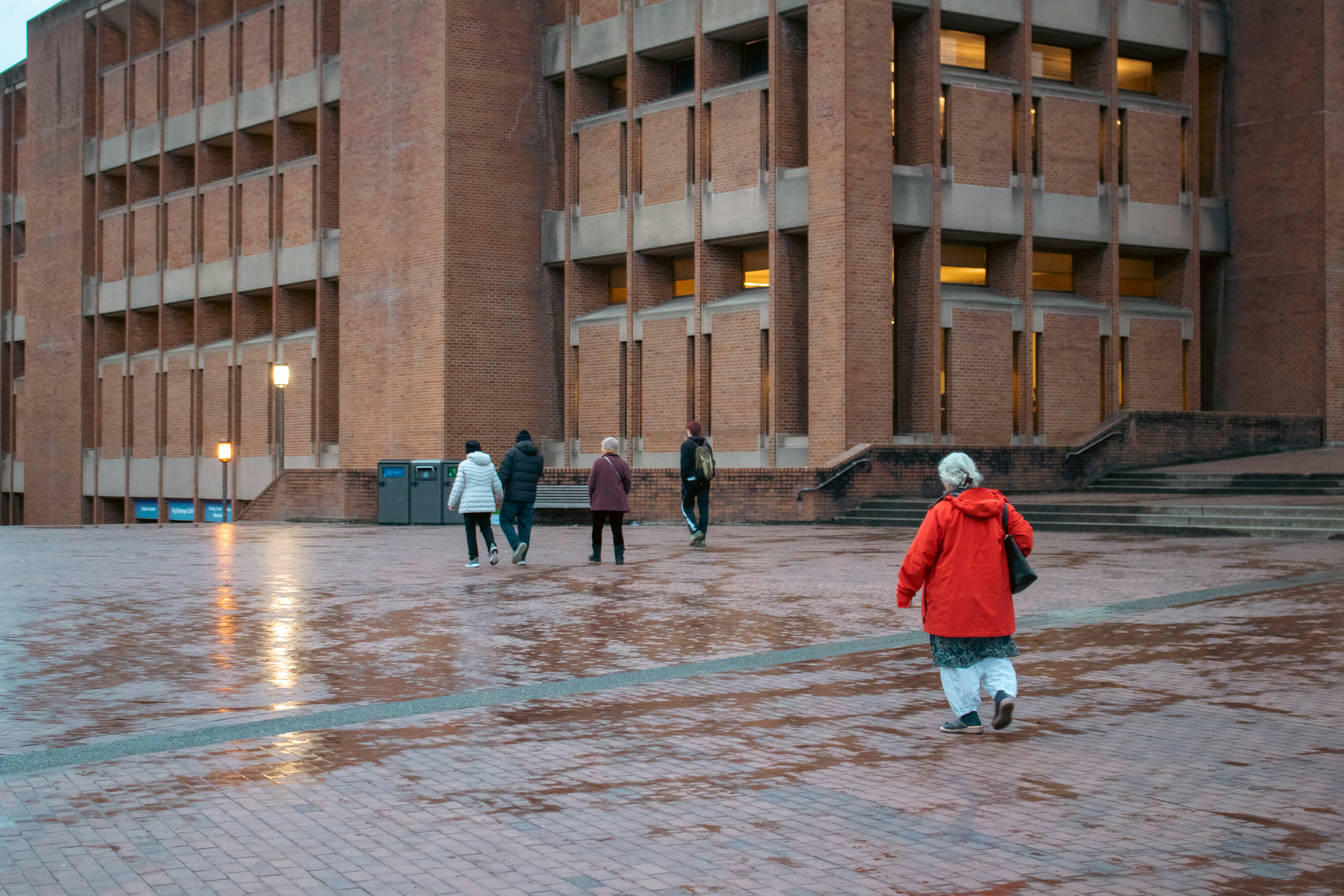 People walk across a wet plaza in front of a building.